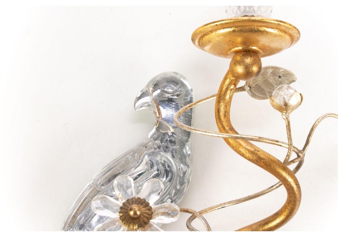Hollywood Regency styling by Italy’s iconic lighting firm, Banci. Crystal opposing parrots perch on shaped crystal urn forms. The twin lights in gilt metal swirl around the parrots with crystal leaves and rosettes on scrolled gilt vines. With gilt