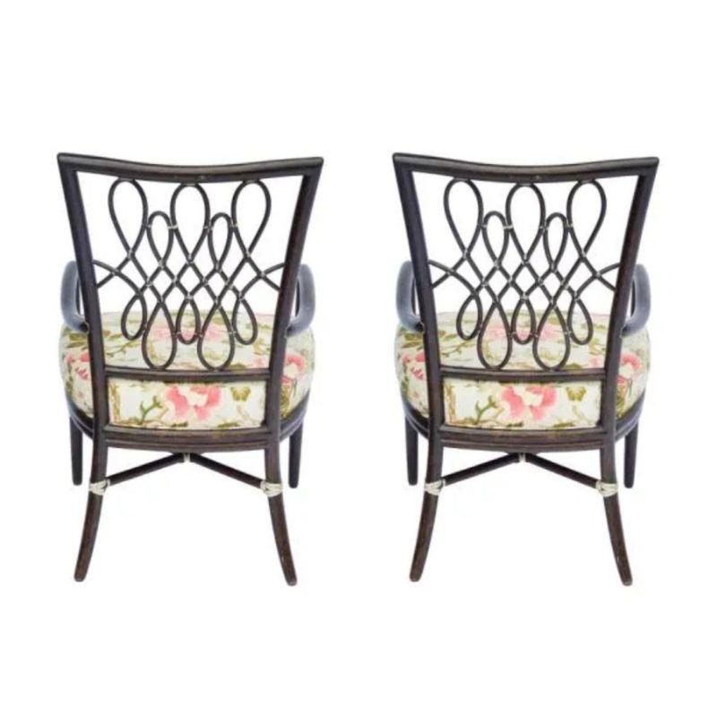 A pair of Barbara Barry for McGuire rattan arm chairs with cheery, floral upholstered seats. The chairs are stained a dark hue with an open curlicue wicker design to the seat back and an X stretcher support to the legs.  The seat cushion is a pink