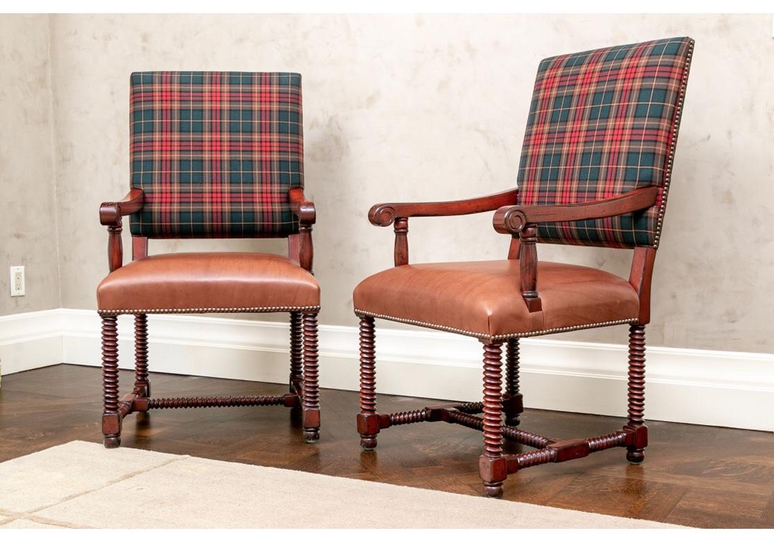 Pair of custom upholstered hall chairs with Ralph Lauren red and green plaid fabric on the backs, and Holly Hunt brown leather seats. The chairs in a reddish brown stain with carved sharp edged barley twist legs, H stretchers, and scrolling