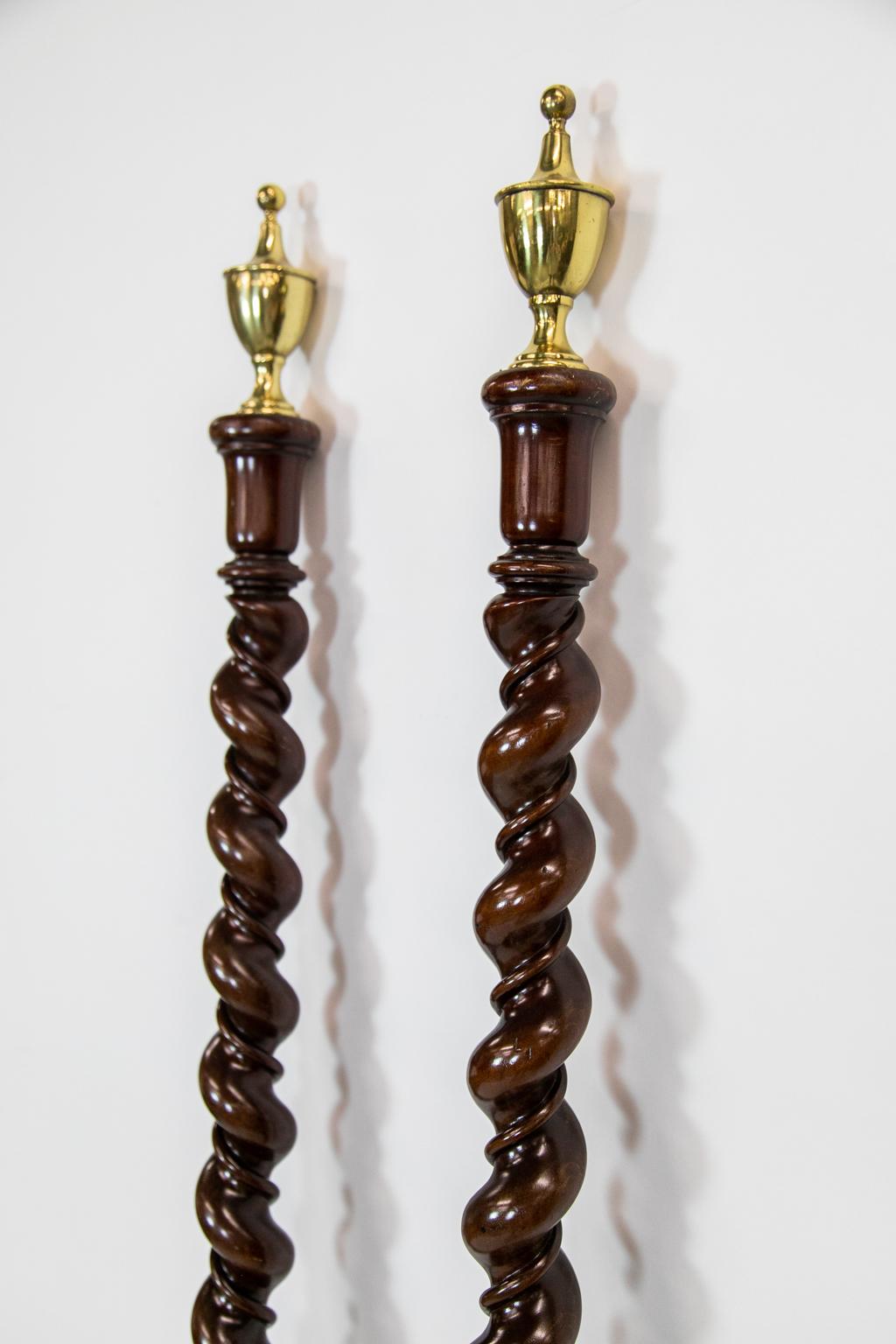 This pair of columns has brass classical urn finials. They have a graduated diameter from top to bottom. The barley twist stem has a continuous carved vine that spirals from top to bottom inside the barley twist. These columns were at some time