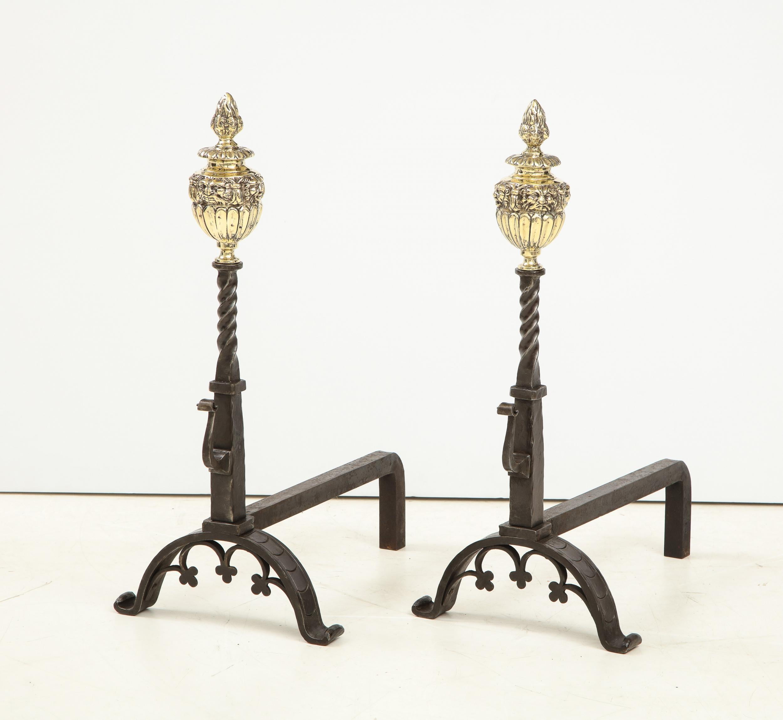Good pair of Arts & Crafts period andirons in the baroque taste, having flame finials with lion mask decorated urns, standing on hammered shafts with etched design, standing on arched legs with trefoil decorated arches.