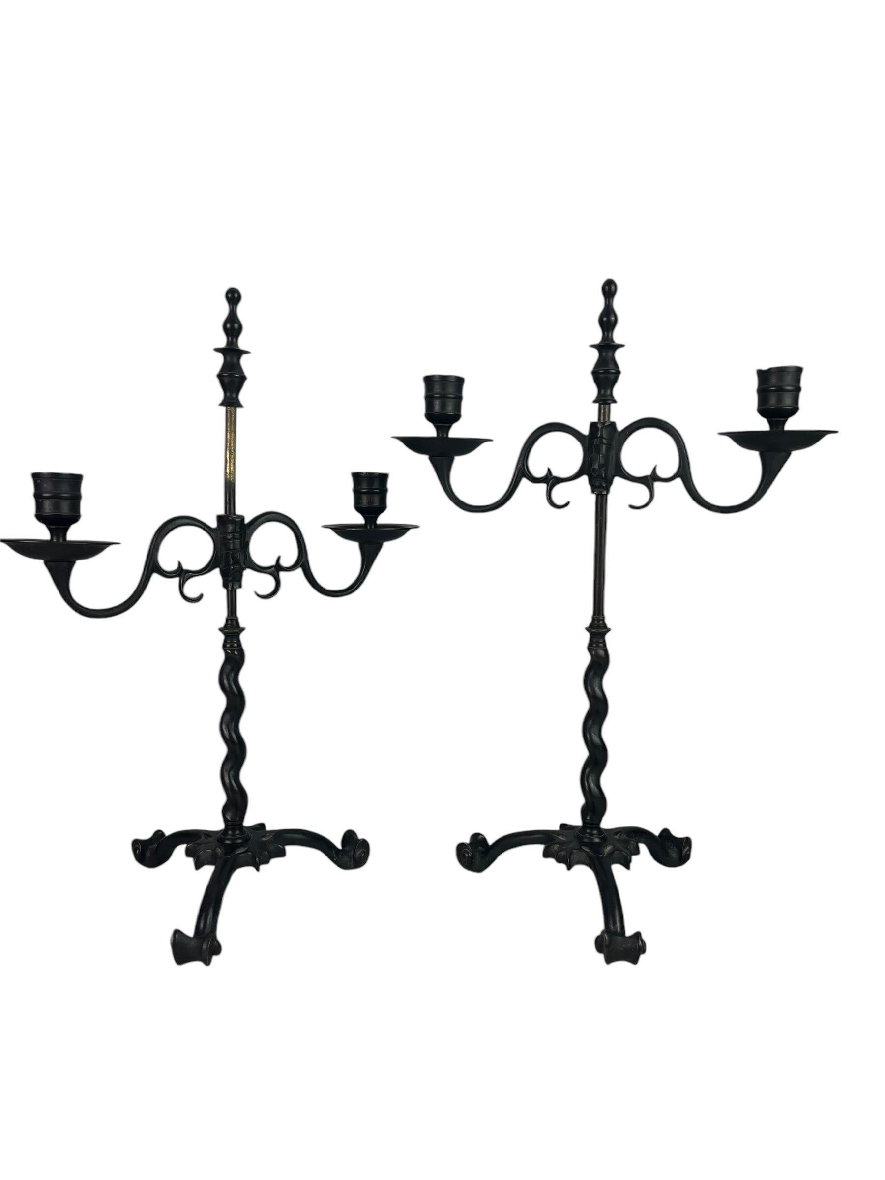 Questa interessante coppia di candelieri in bronzo combina l'eleganza del barocco con influenze gotiche e rinascimentali. La base a tripode, rifinita con volute, è sormontata da un fusto contorto che continua con una parte liscia di 13,5 cm (circa