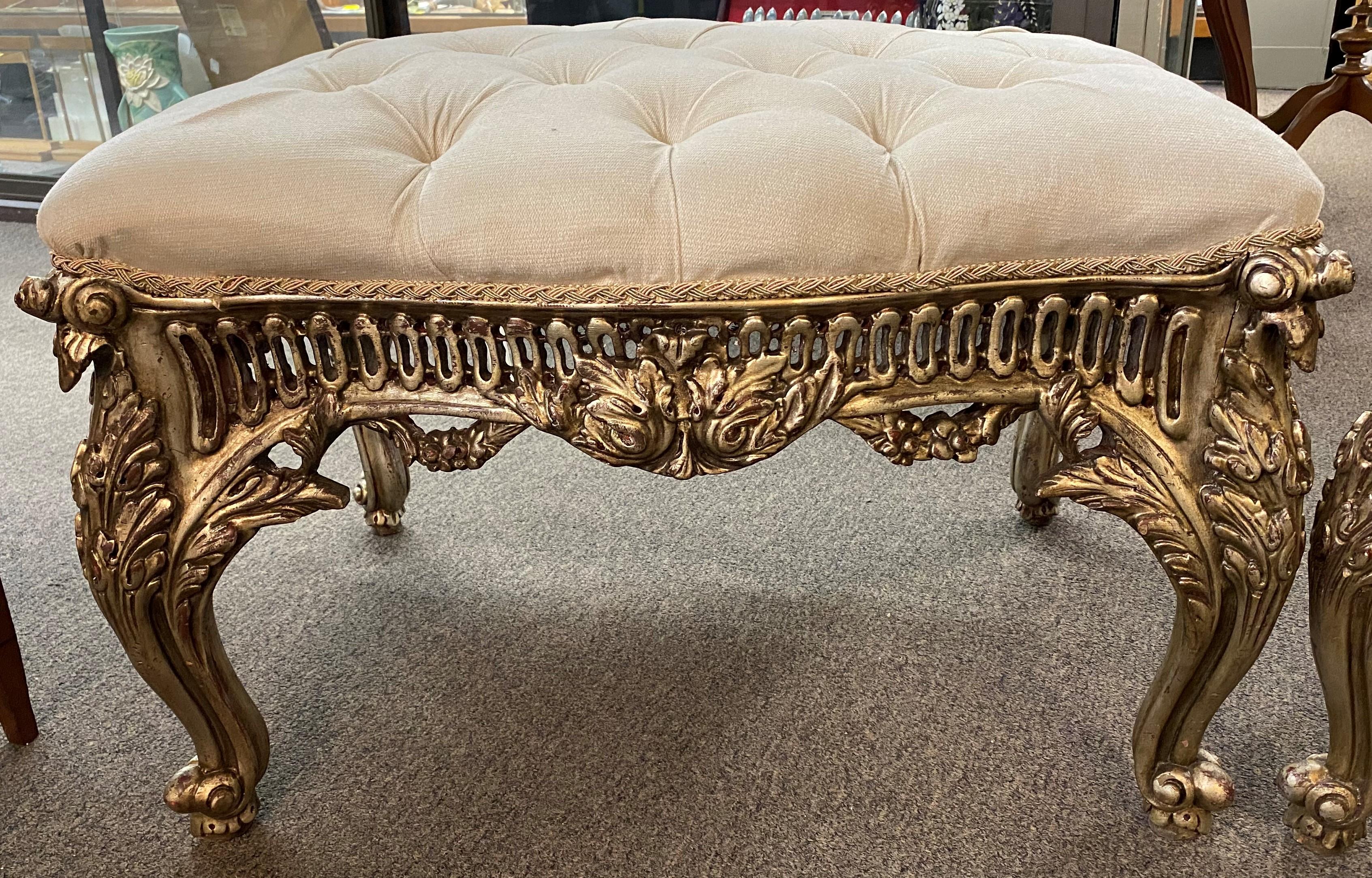 A decorative pair of Baroque or Rococo style wooden pierce carved silvered ottomans with foliate and scrollwork cabriole legs and tufted light gray upholstered cushions, dating to the 20th century. Very good overall condition with minor