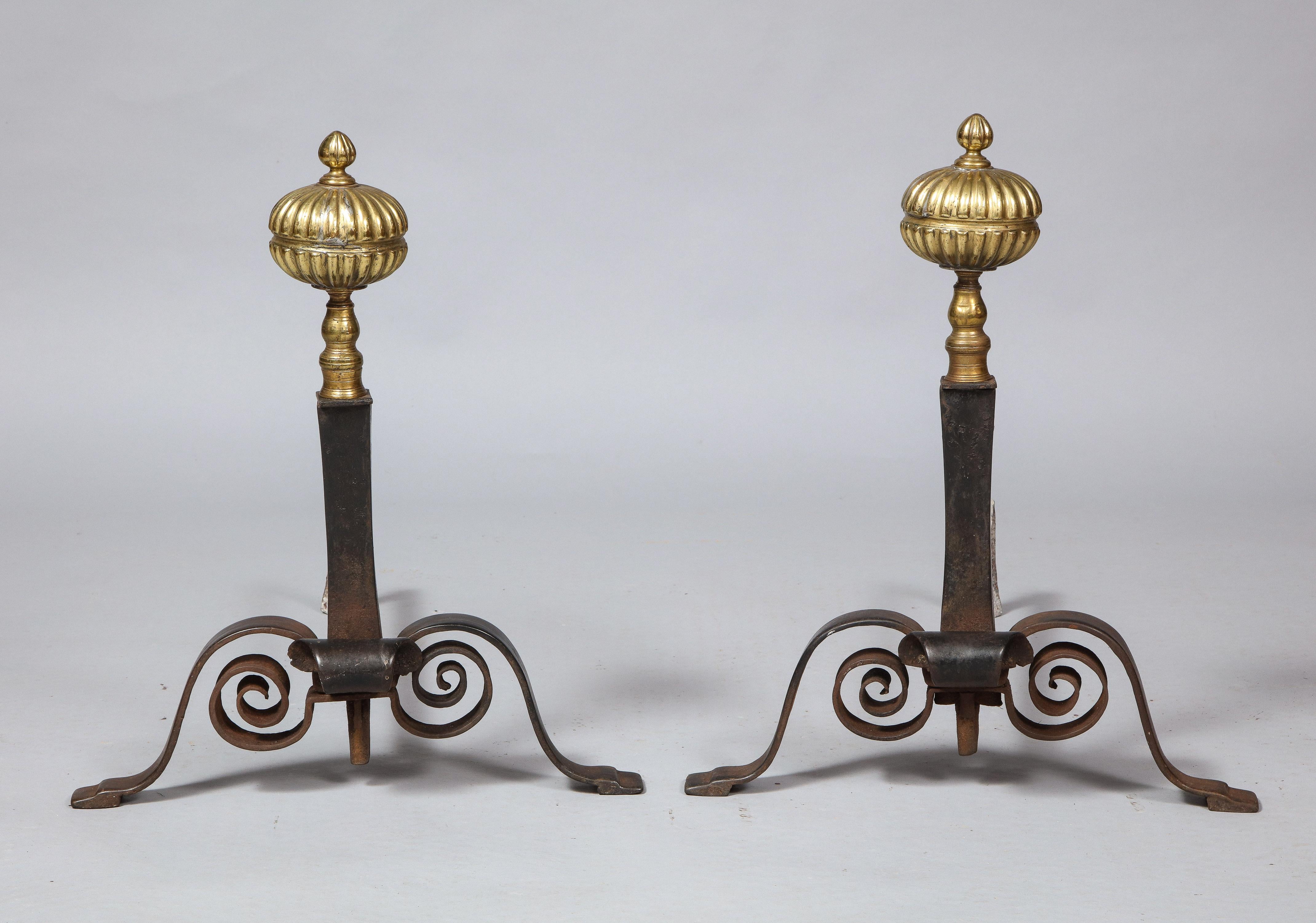 Good pair of Arts & Crafts period brass and wrought iron andirons, the onion finials with ribbing and central turned channel, over tapering shafts standing on scrolled legs and stepped feet.