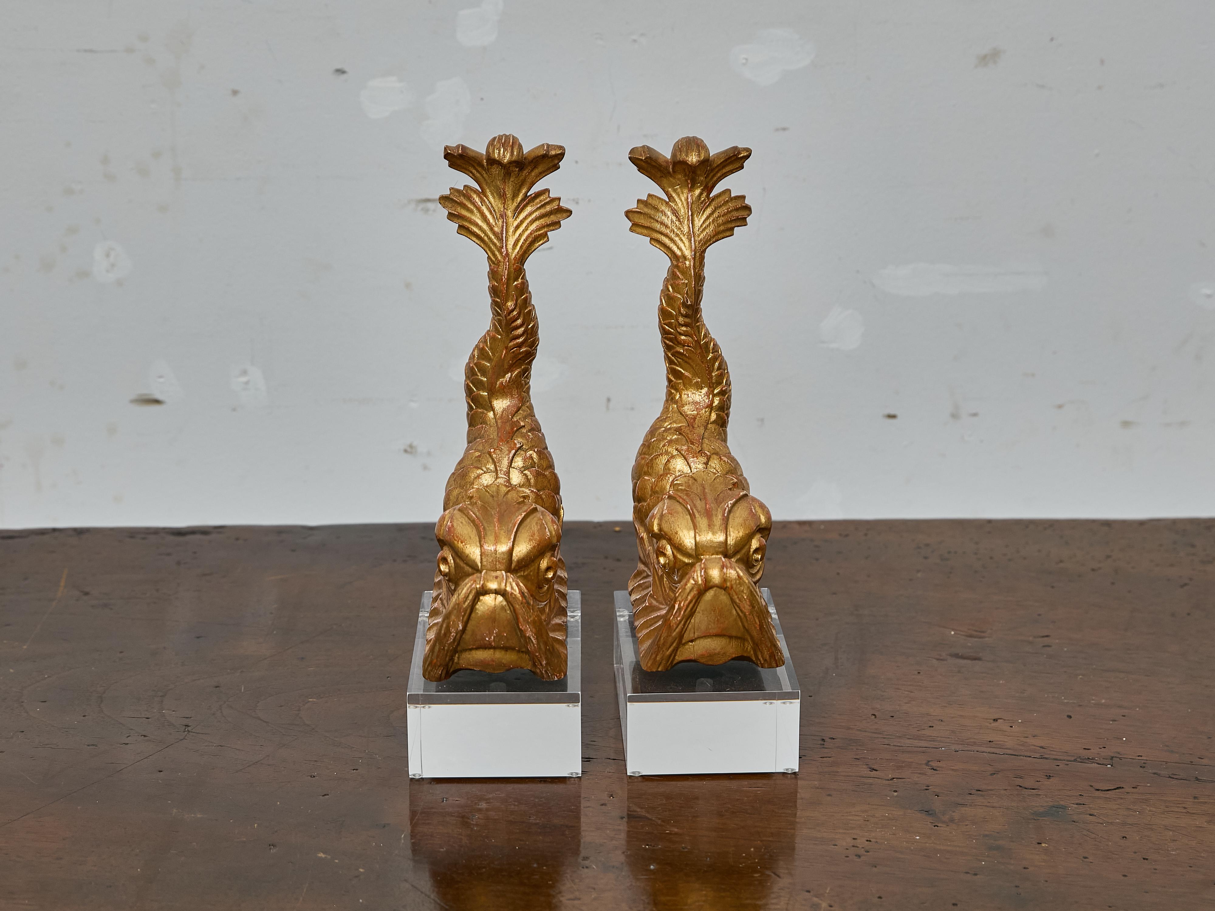 Questa straordinaria coppia di figure di delfini in legno dorato intagliato, montate su basi in lucite trasparente, è probabilmente nata come elemento architettonico decorativo - forse una volta adornava un mobile, una boiserie o un grande