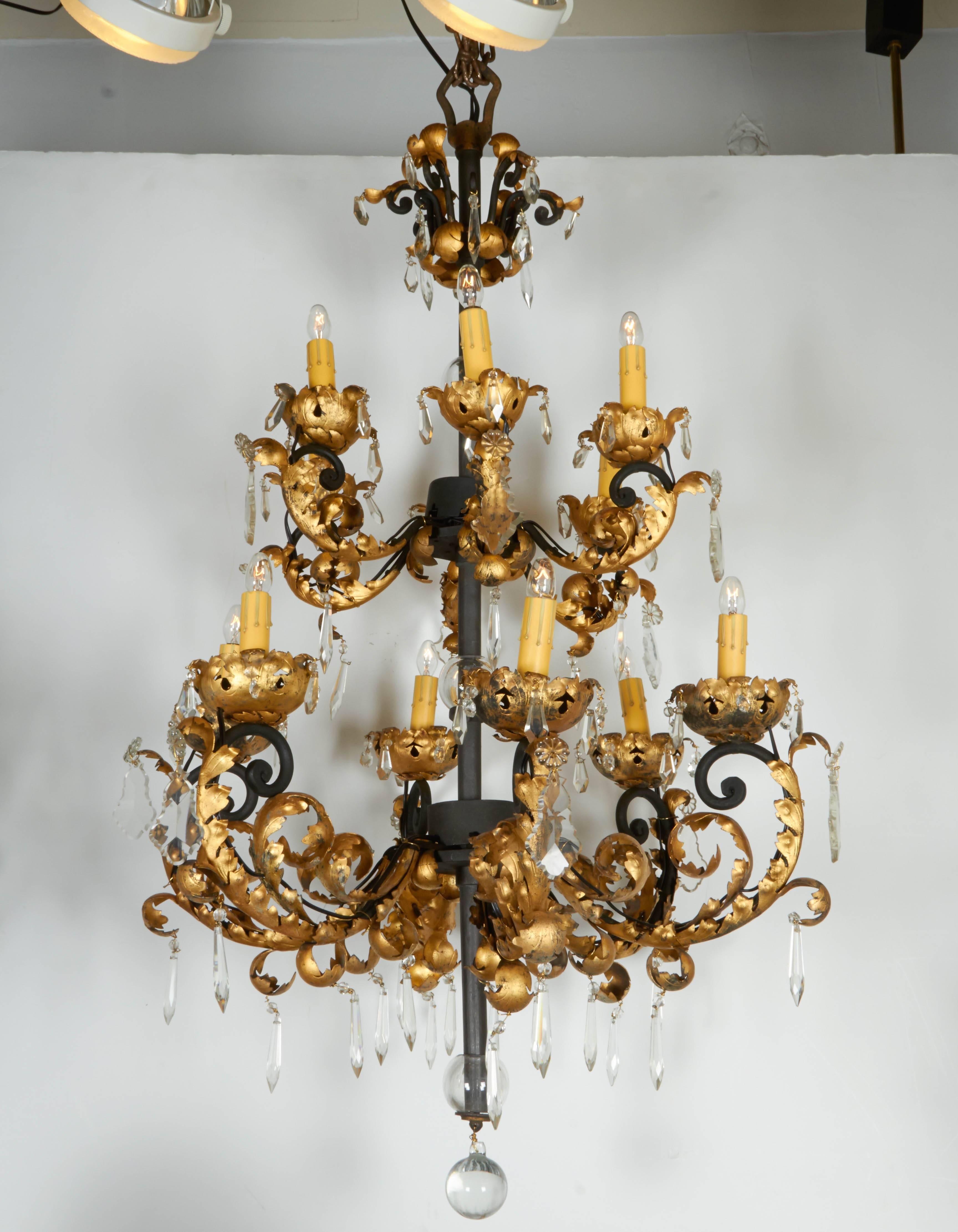 A dramatic pair of Baroque style Hollywood Regency black satin enamel and gilt chandeliers with crystal accents, circa 1950, each chandeliers has 12 lights, pointed and flat cut crystals and ball pendant. Handwrought and gold leafed. Nearly