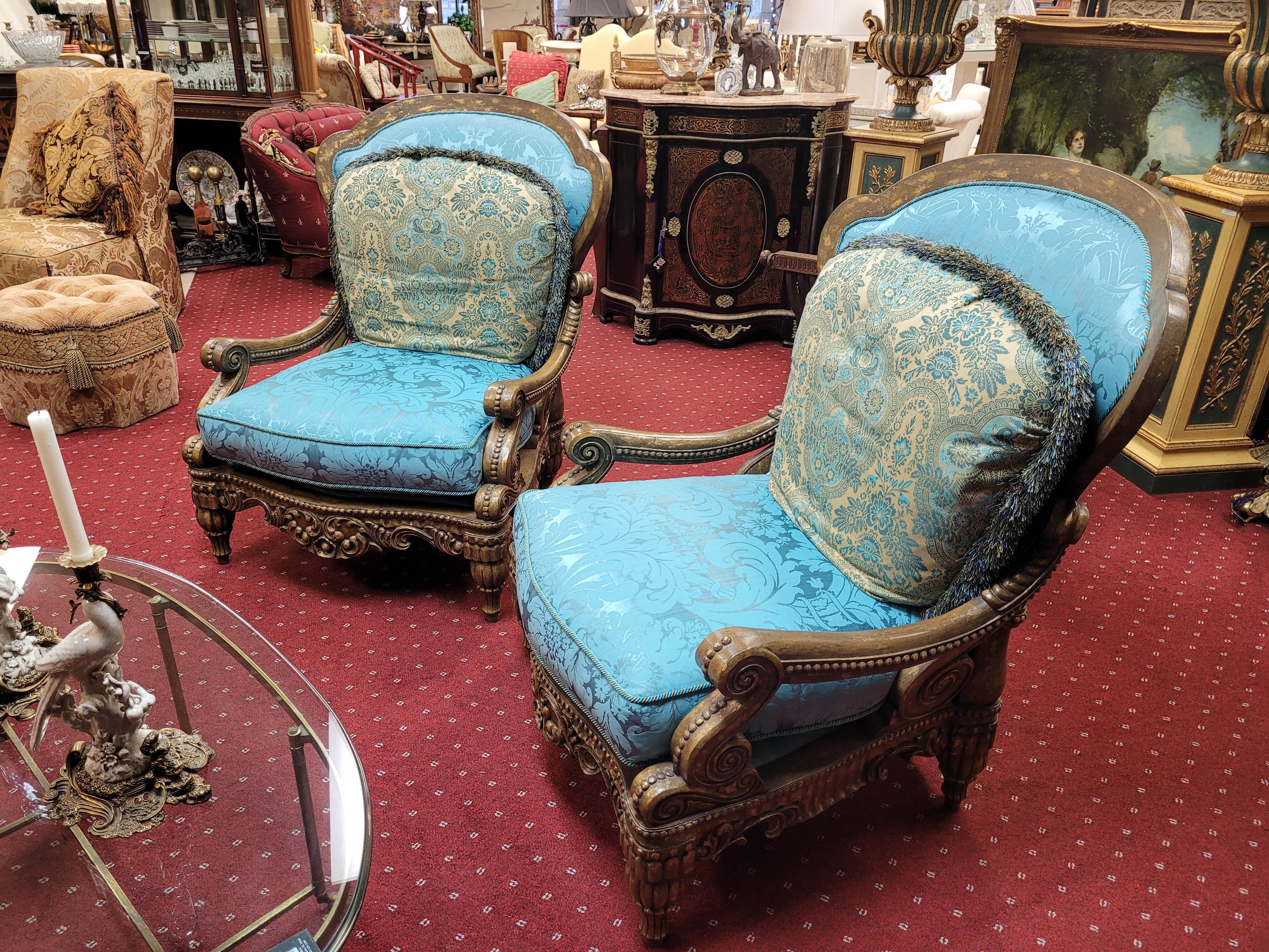 A gorgeous pair of baroque-styled oversized arm lounge chairs by Tomlinson, upholstered in a captivating iced blue sateen damask textile. The chairs feature a solid wood frame and are carved with intricate details finished in antiqued gold. Whether