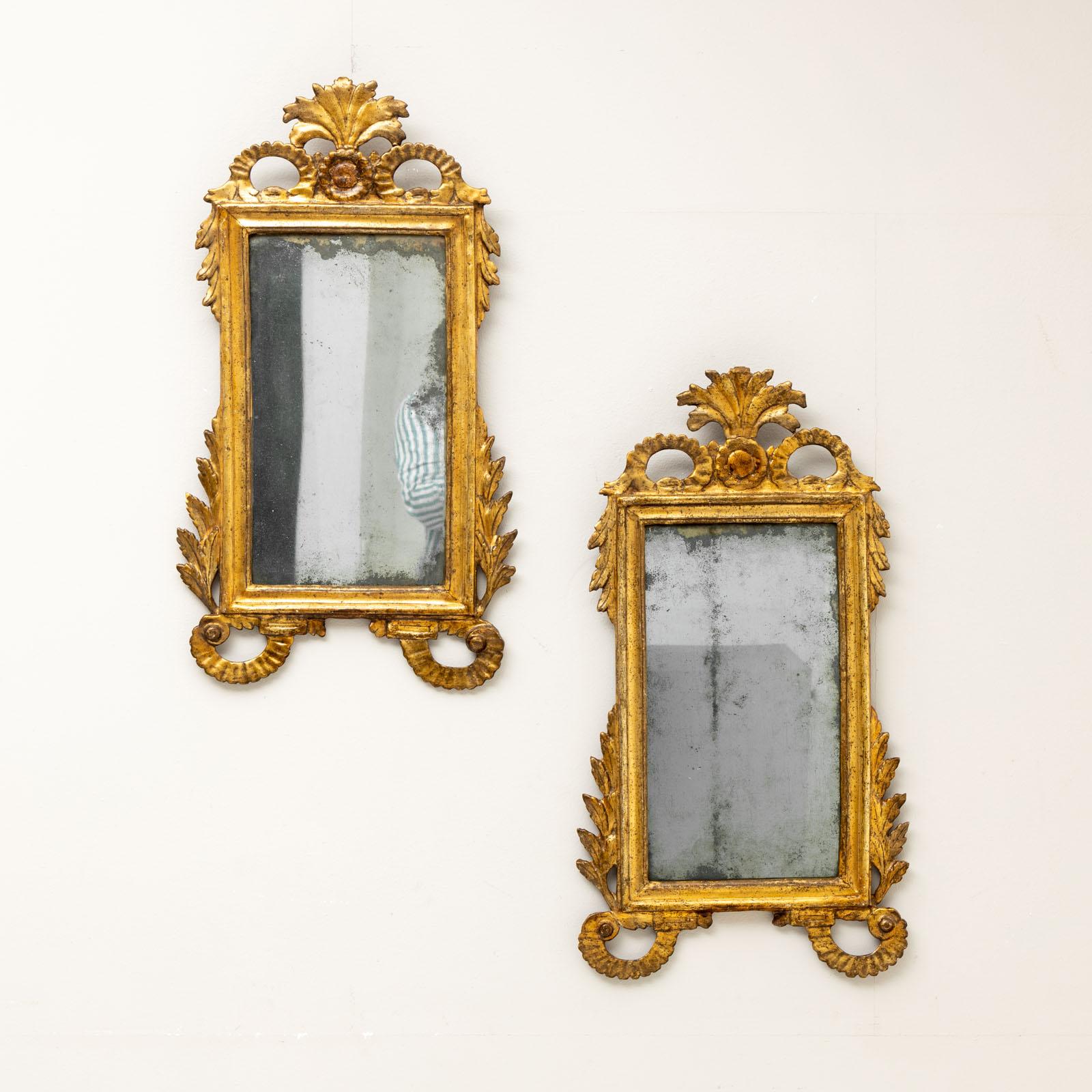 Paire de miroirs muraux en bois doré de format rectangulaire avec des décorations de rocailles et de feuilles autour de la moulure profilée. Le verre du rétroviseur est vieux et présente des angles morts. La dorure est en bon état, de facture