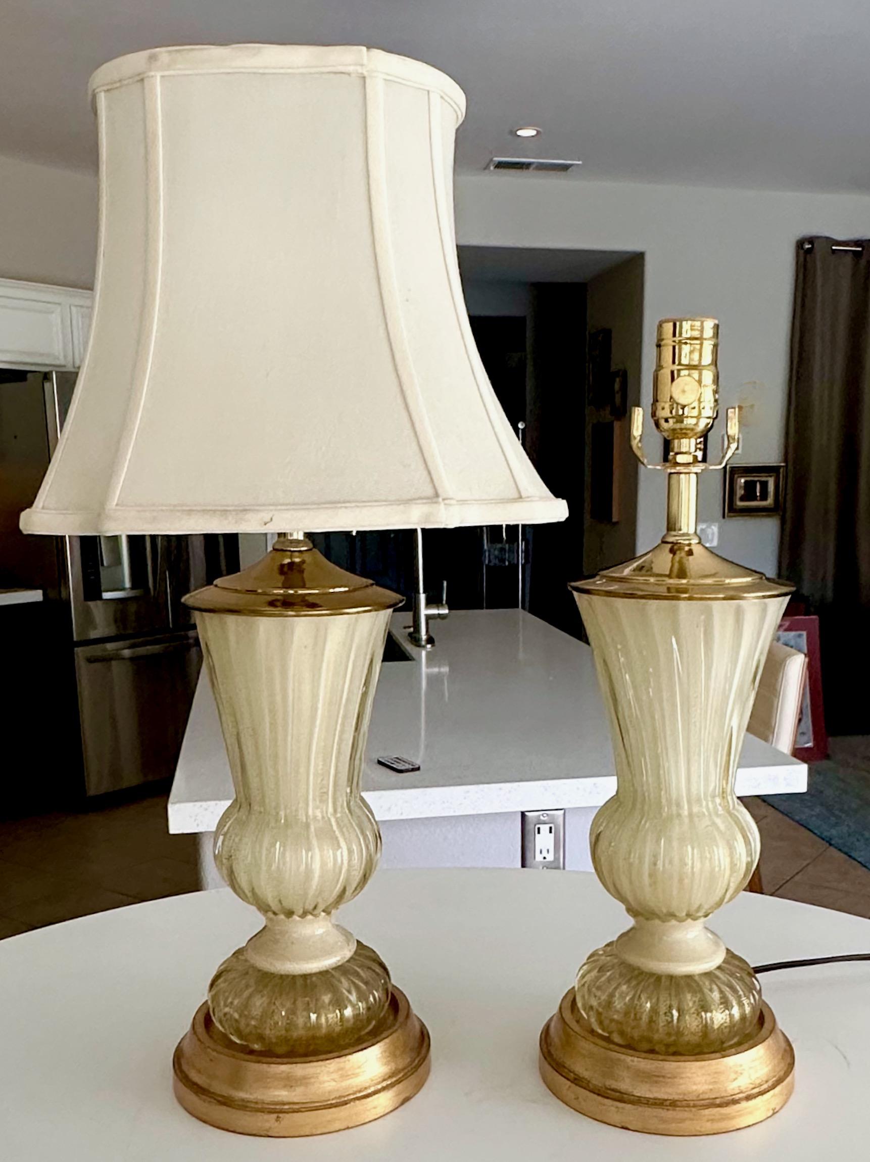 Coppia di lampade da tavolo di Murano in scala ridotta, soffiate a mano, color crema e con inclusioni dorate, di Ercole Barovier&Toso. Montati su basi in legno dorato. Cablata di recente con nuove prese a 3 vie in ottone e cavo.
La parte in vetro