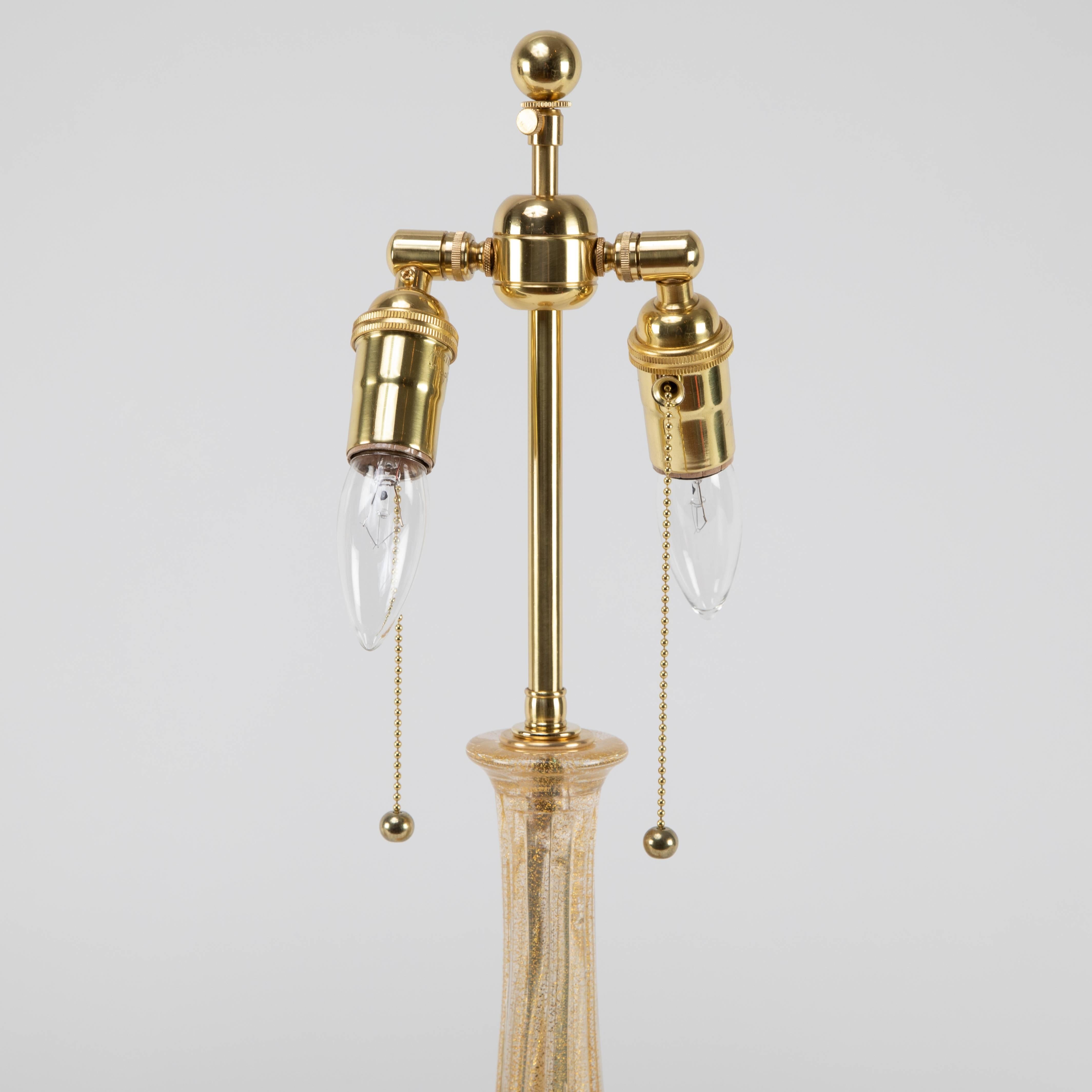 Stunning pair of  table lamps with gold-accented Murano glass. Each lamp features a twisting and tapered stem resting on a flared base. The hand-blown glass has a ribbed surface with gold rope inclusions on the inside of the ridges. Each lamp uses