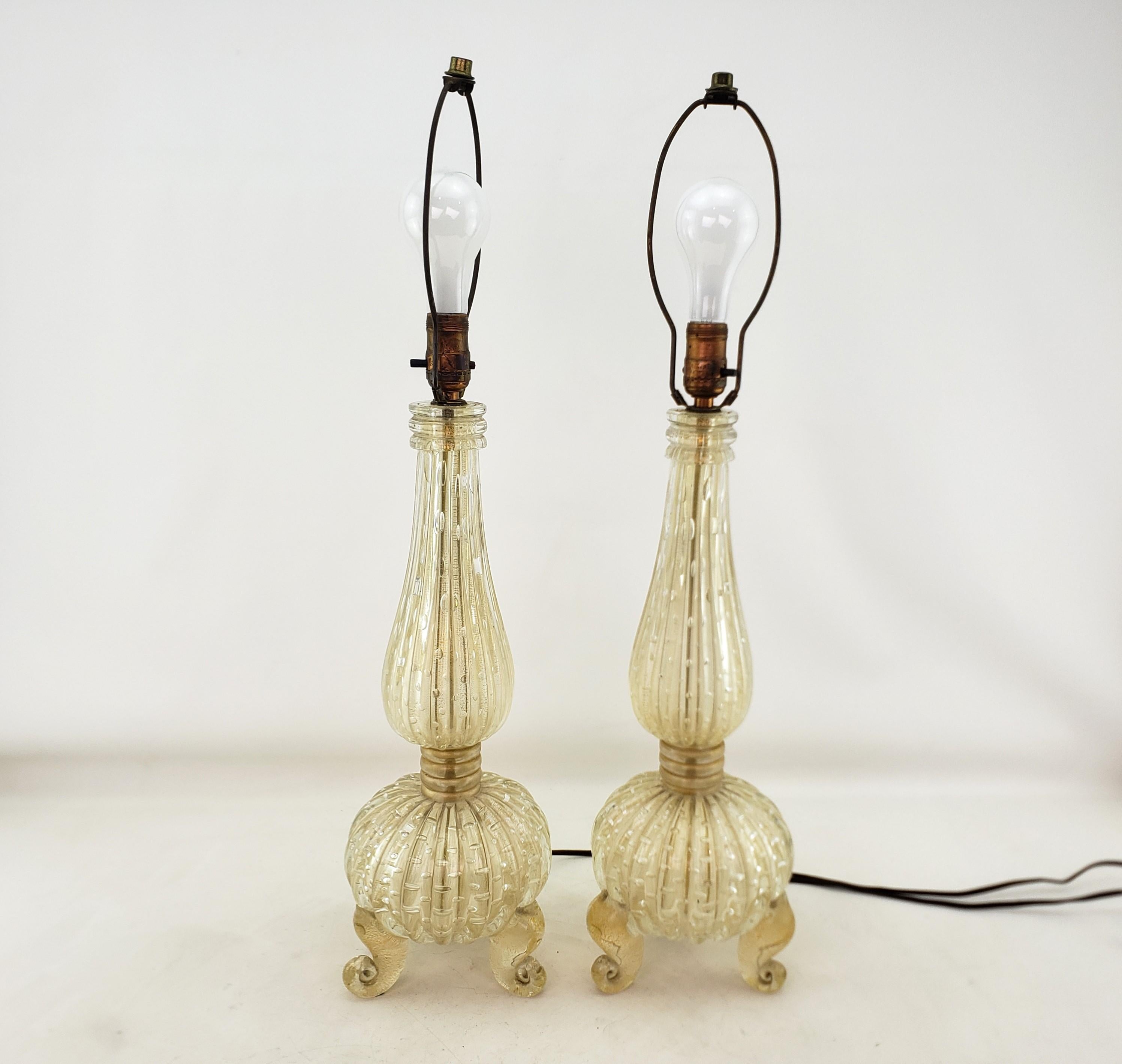 This pair of table lamps are unsigned, but being attributed to Barovier of Murano Italy and date to approximately 1950 and done in the Mid-Century Modern style. The lamps are composed of a heavy clear art glass with ribbed stems and bulbous bases