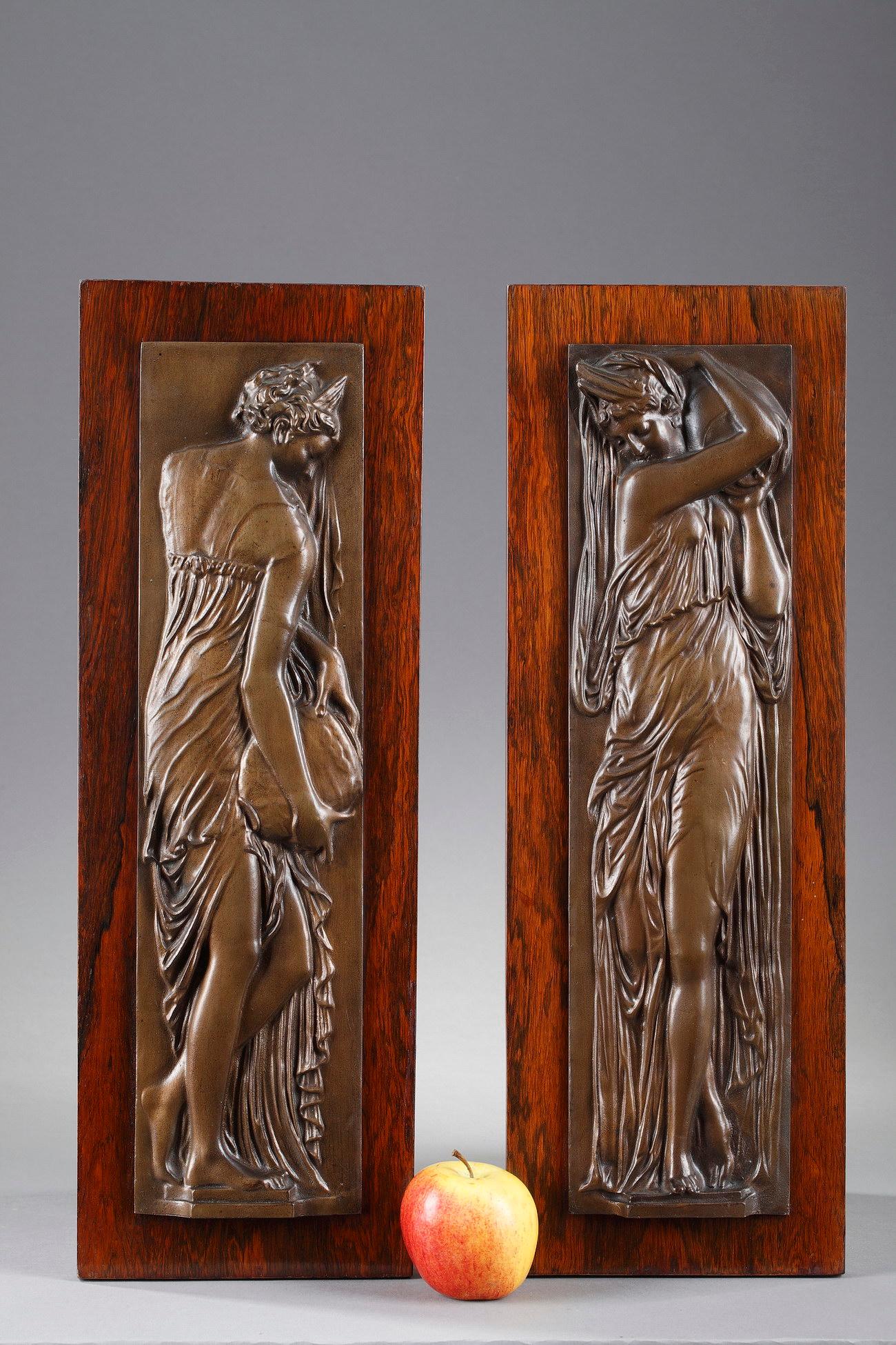 Pair of bronze bas-relief from the end of the 19th century, with brown patina, fixed on a wood veneer support, representing two women draped in the antique style carrying a jar. One is delicately pouring water from her jar, and the other, is