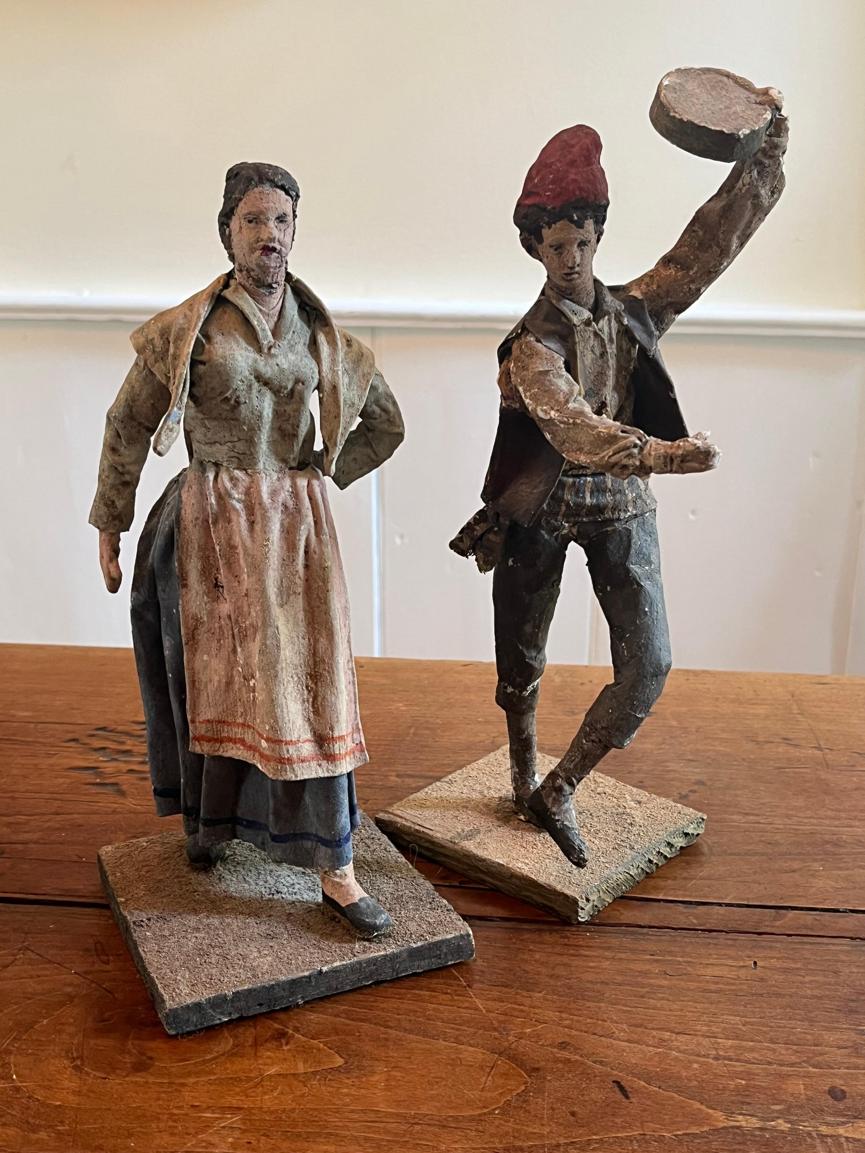 Pareja de figuritas de cuna de papel maché que representan a campesinos vascos vestidos de época, el hombre bailando con una pandereta y la mujer con un delantal. 