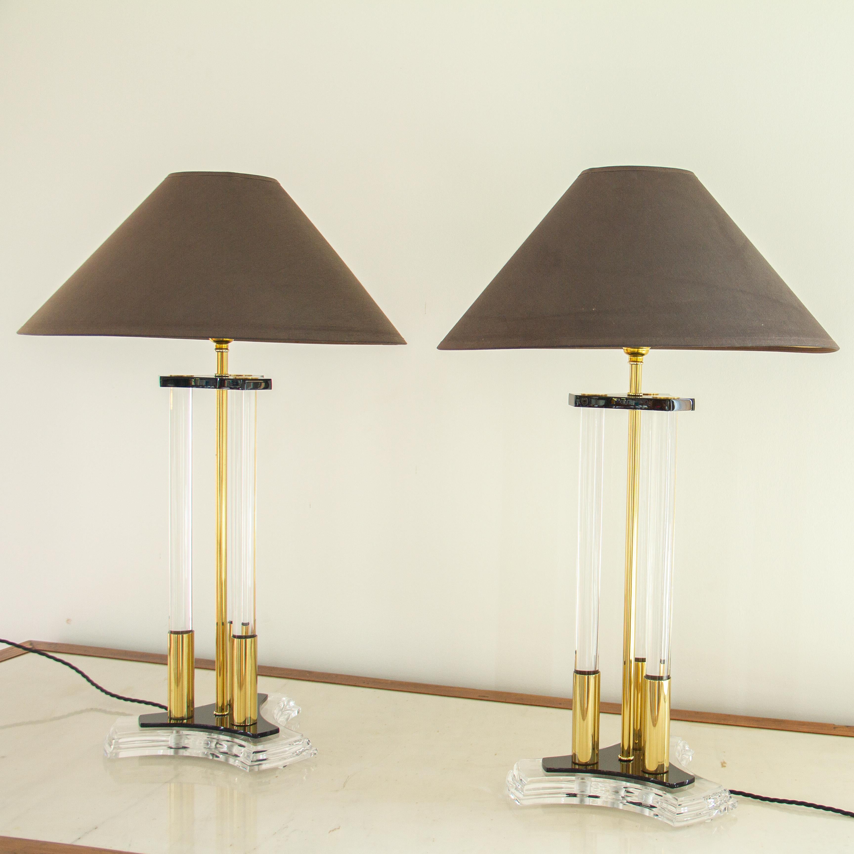 A pair of brass, acrylic and Lucite lamps with three Lucite tubes wrapped in brass and surrounding a brass stem. The tubular supports sit on top of a black acrylic plate atop a Lucite horned triangle. The lamps have been paired with stitch detail