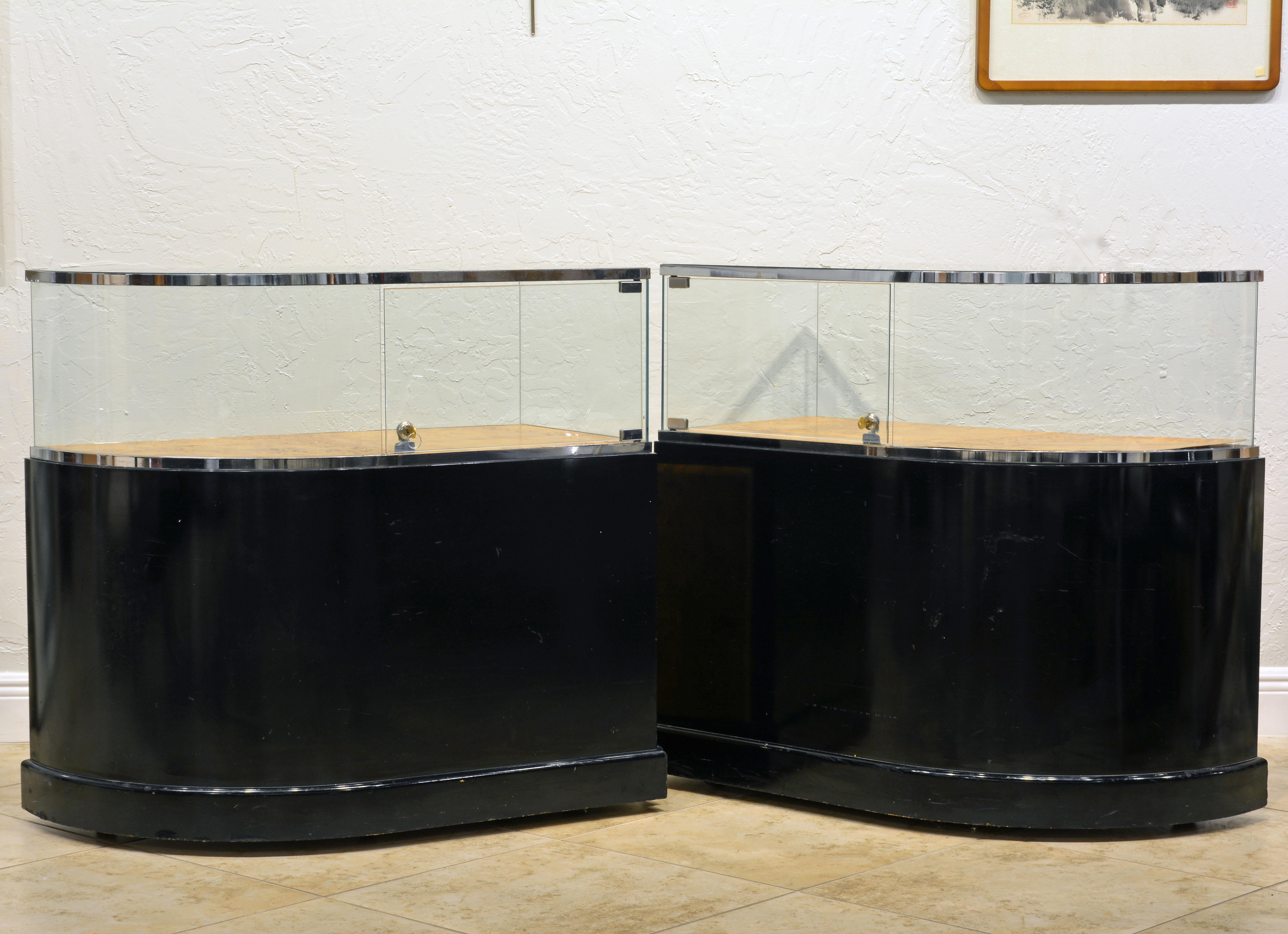 This pair of Minimalist styled display counters with rounded ends feature and elegant top glass and chrome section with burled wood floor above a black lacquered body adorned with burled wood panels and cabinet doors. The design reflects the