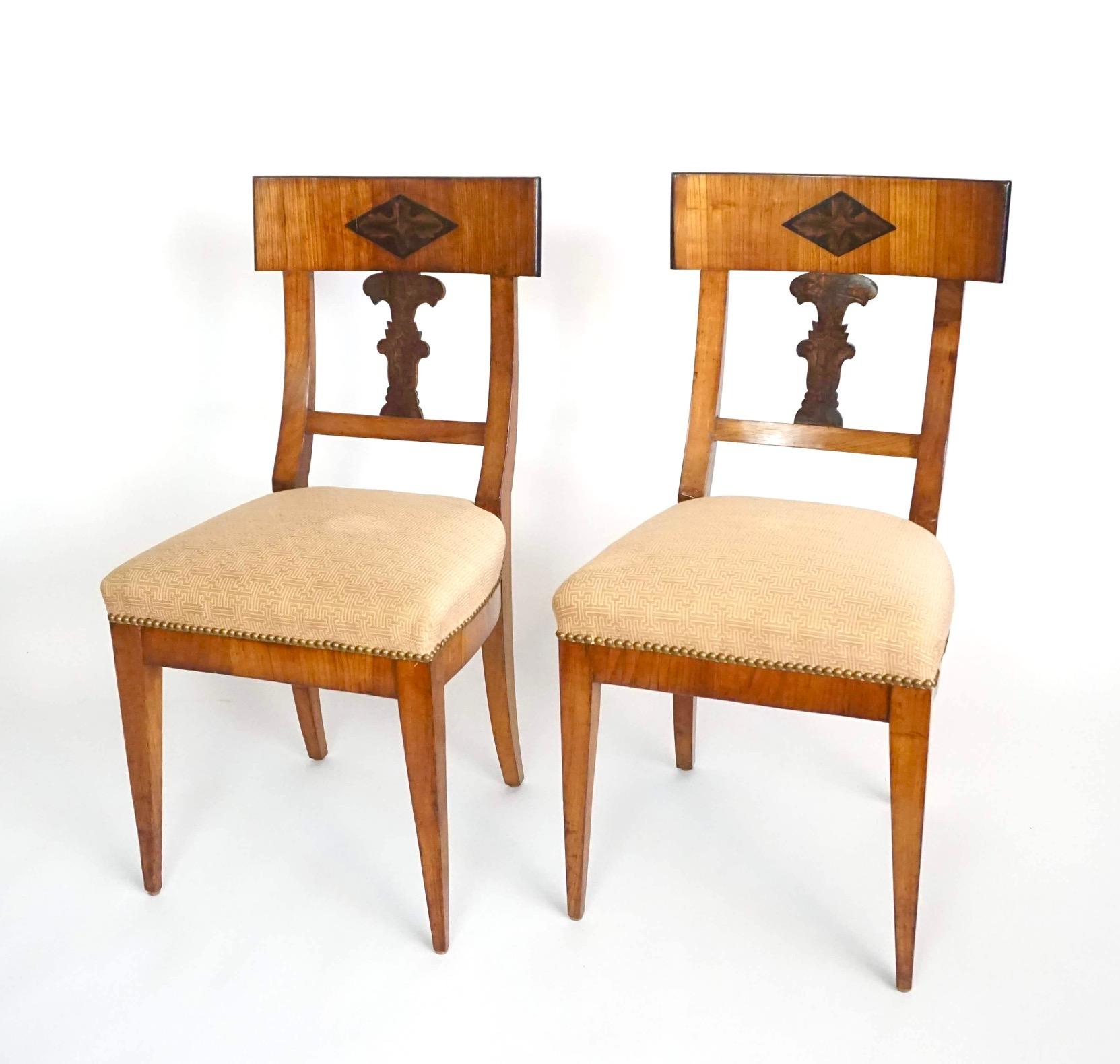 An attractive pair of circa 1820 Bavarian Biedermeier side chairs of large scale having walnut frames, the curved crestrails with center penwork acanthus lozenges and shaped backsplats with penwork foliate designs above 