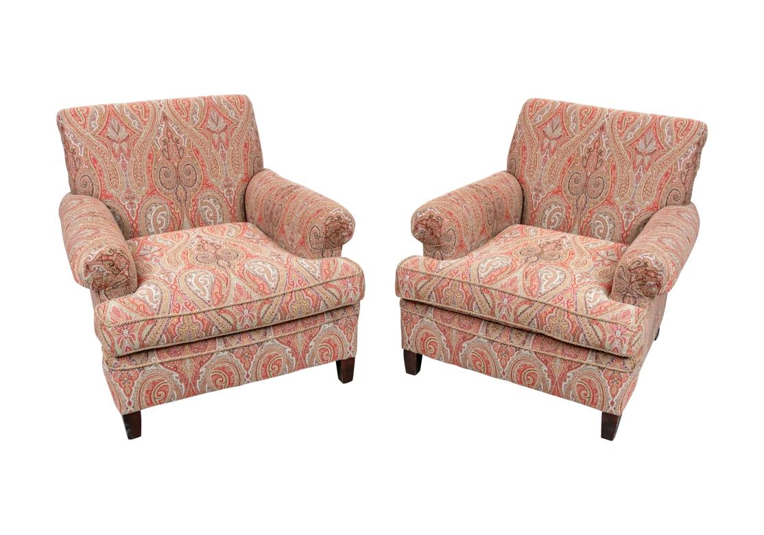 A finely constructed pair of club chairs upholstered in a machine paisley fabric in a classic Kashmir pattern in red with tan, brown and white. The chairs with sloping scrolled backs and scrolled pleated arms. The seat cushions with coordinating