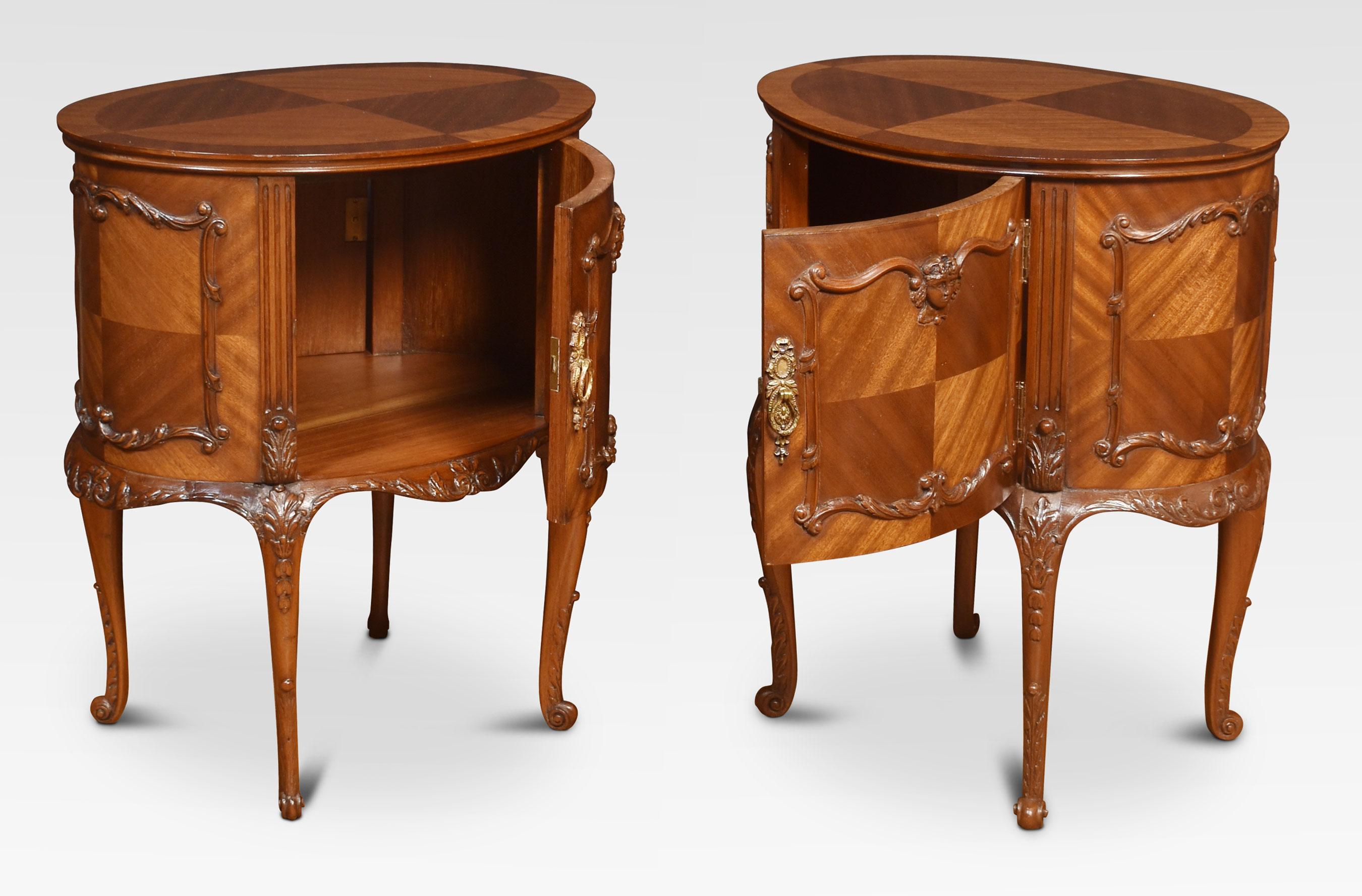 Pair of Louis XV-style oval double-sided night tables/ bedside cupboards, each with quartered and crossbanded tops above doors at opposing sides both with carved and moulded decoration supported on slender cabriole legs terminating in scrolling
