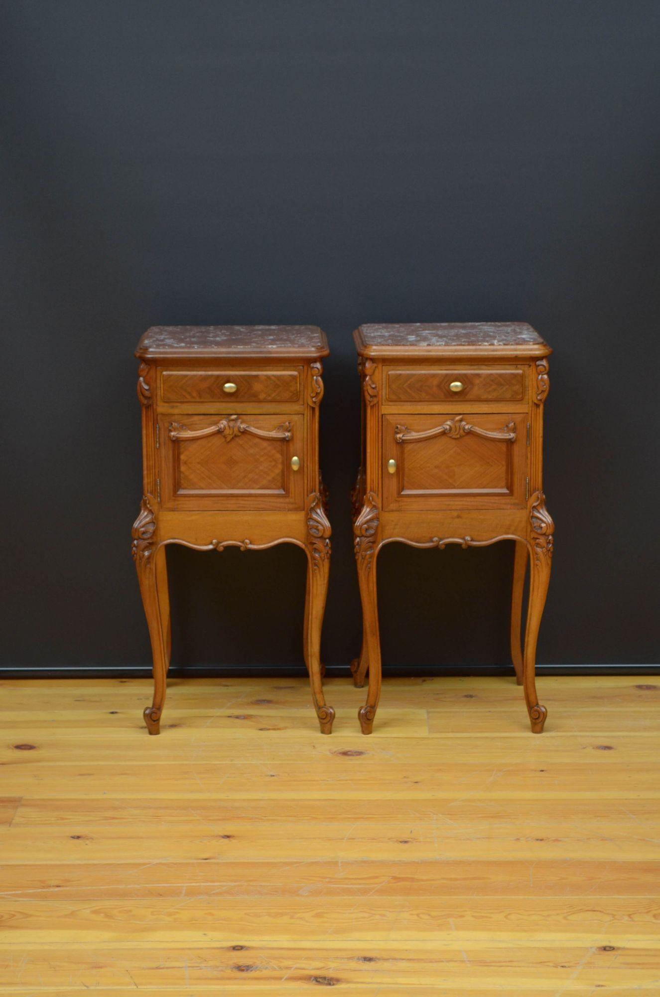 Sn5258 An attractive Continental pair of walnut bedside cabinets, each having red veined marble top above a side slider, panelled drawer and cupboard door with scroll moulding flanked by leaf carvings and fitted with brass handles, standing on