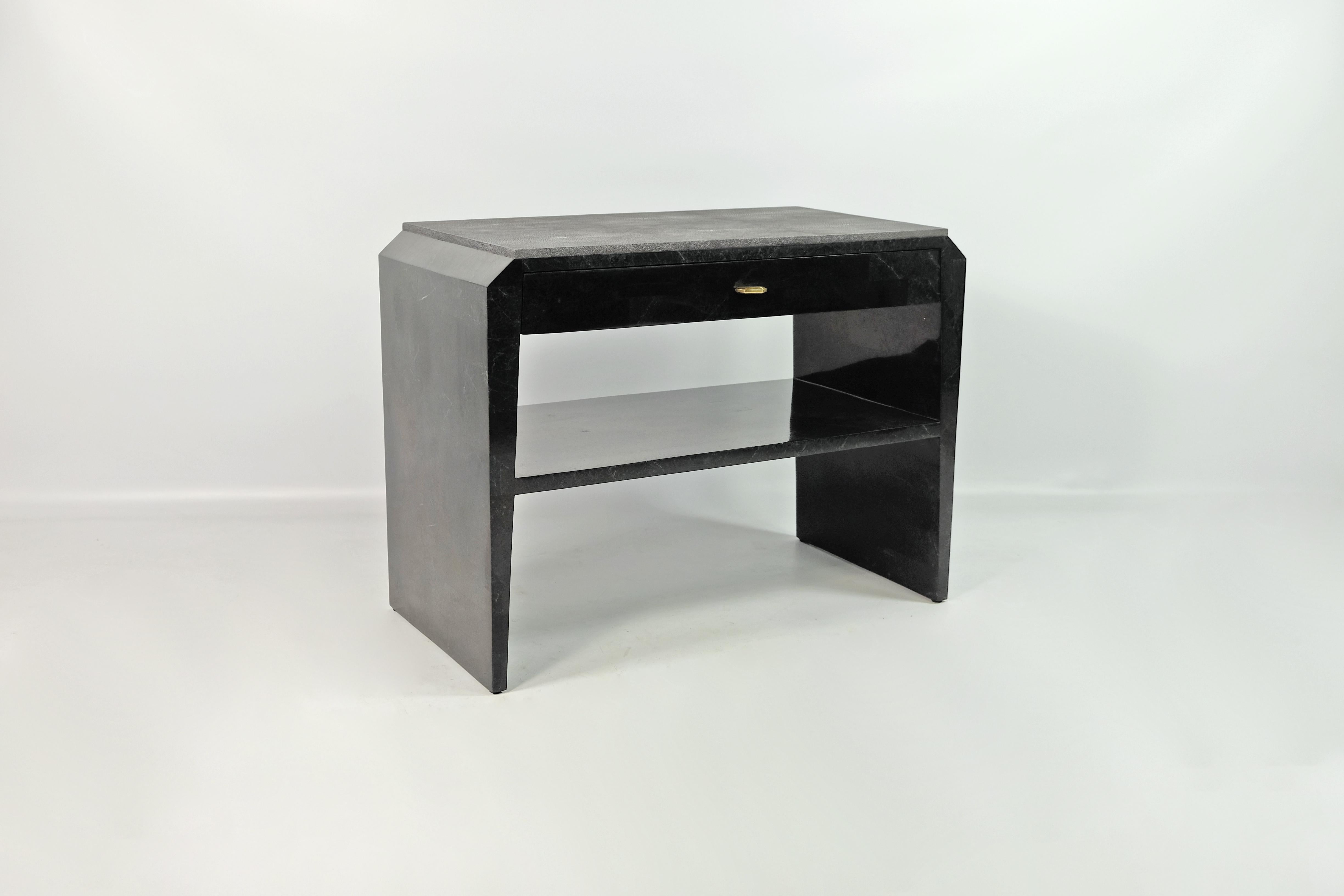 Cette paire de tables de chevet est réalisée en marqueterie de pierre noire (granit) avec un plateau en galuchat.
 
Il y a un tiroir avec un intérieur en placage de bois foncé, et une étagère en pierre noire.
Les boutons sont en laiton avec une