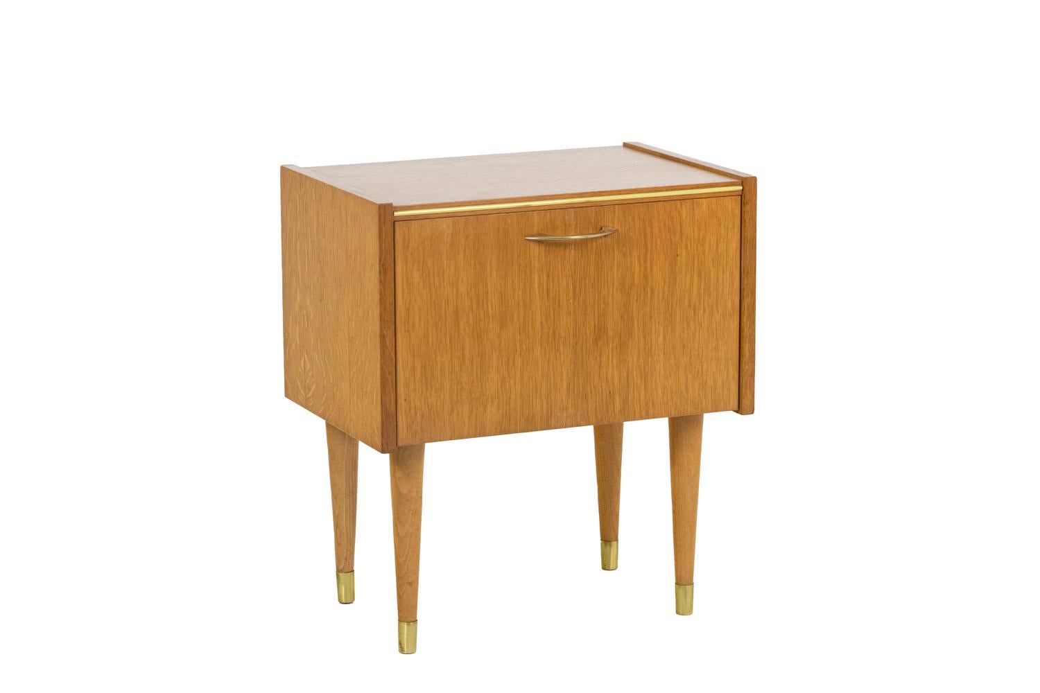 Semb, edited by. 

Pair of bedside tables in blond oak, tapered legs ending in brass finishes. A central door opening downwards. Inside, the top of each foot is marked with a red stamp “S.E.M.B. registered model.” Rounded brass cuffs.

French
