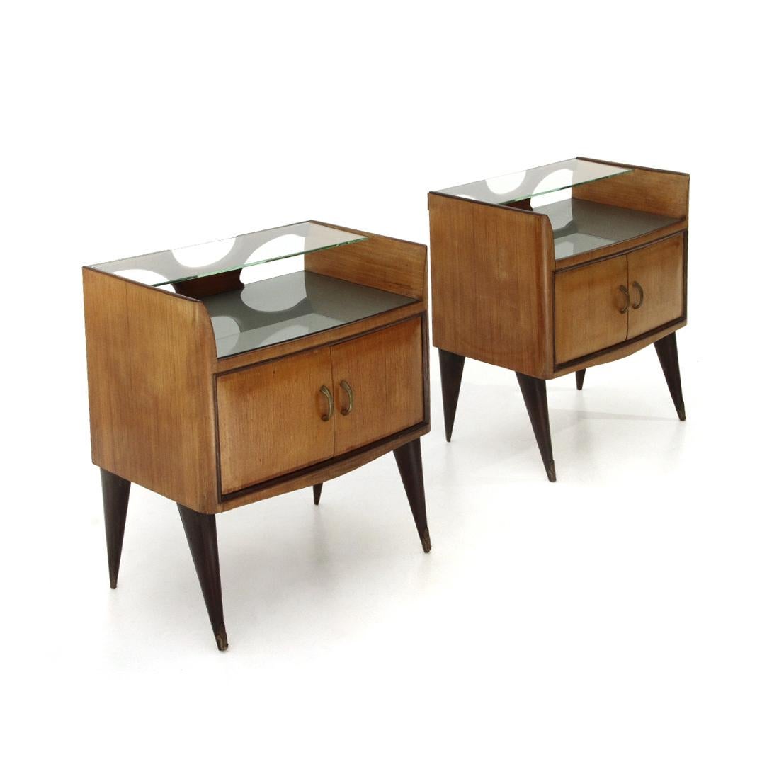 Pair of Italian-made bedside tables produced in the 1950s.
Structure in veneered wood.
Storage compartment with brass doors and handles.
Back-painted glass top.
Upper shelf in transparent glass.
Legs in dark brown stained wood with floral brass
