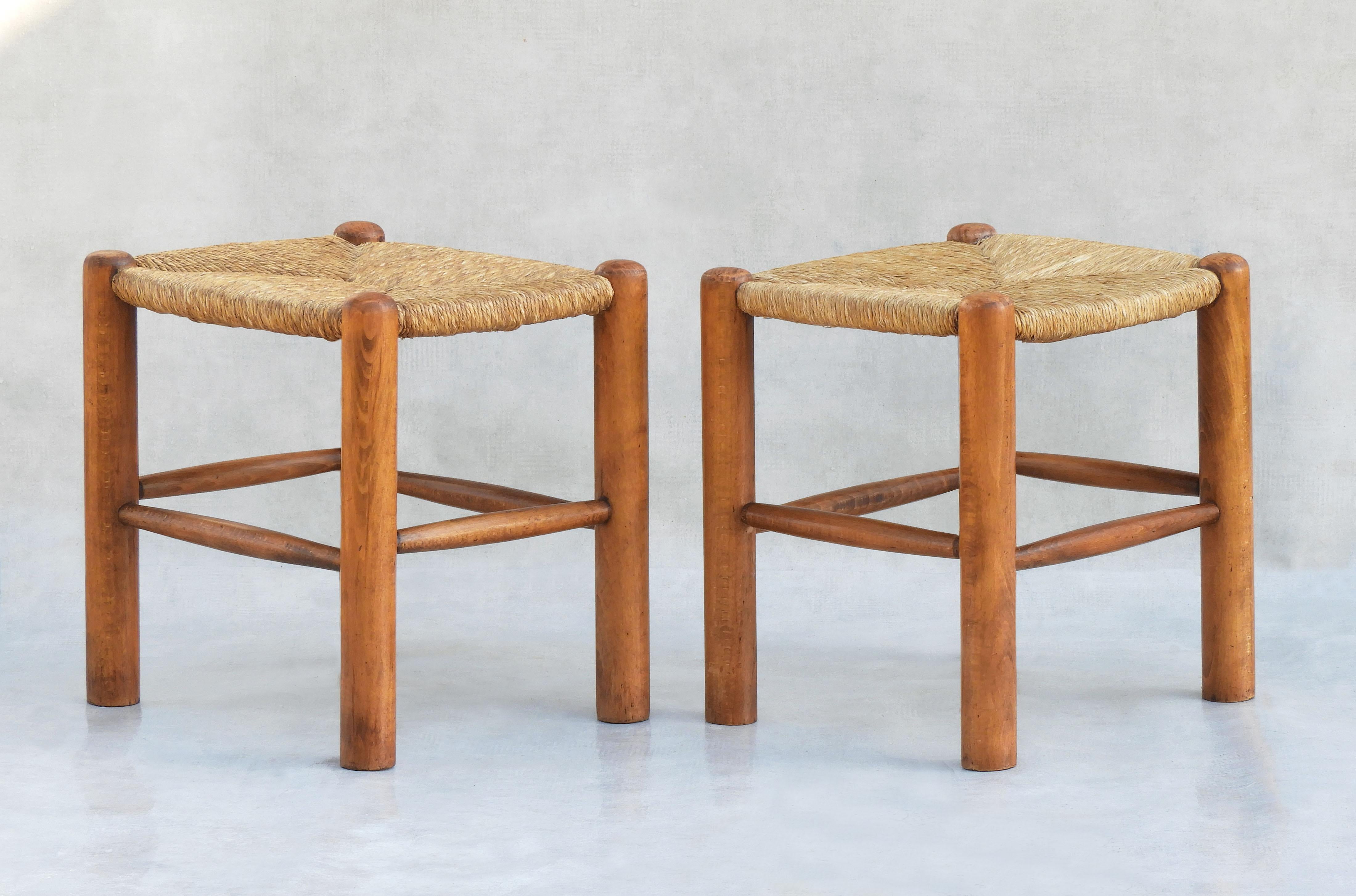 Paire de tabourets de style Charlotte Perriand, circa 1970 France.
La quintessence du design provincial français avec une touche de modernité du milieu du siècle.  Assise en jonc tissé neutre sur une structure en bois de Beeche tourné. En bon état