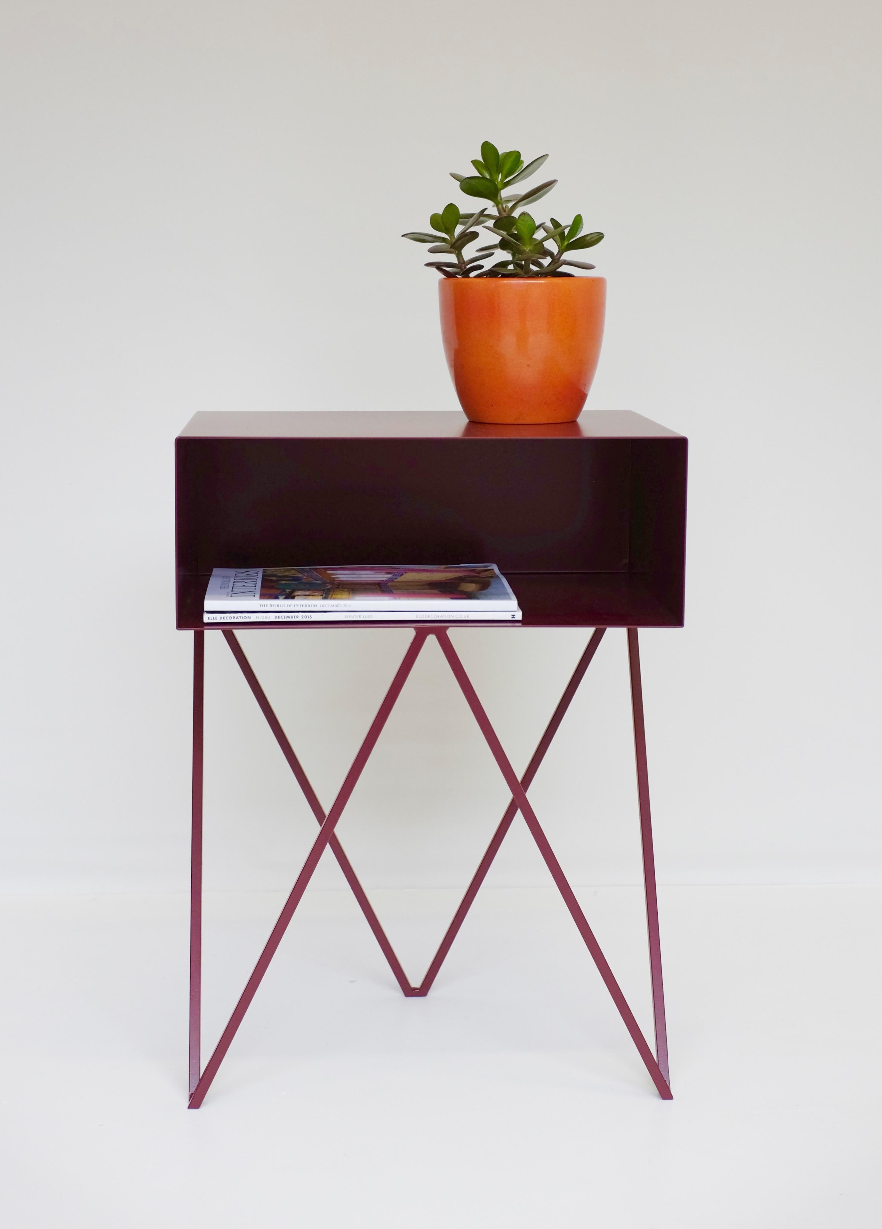 A pair of burgundy powder-coated steel robot bedside tables. The Robot side table features an open shelf on zig zag legs. A fun and functional design made of solid steel, powder-coated in blueberry. The clean lines look great against period details