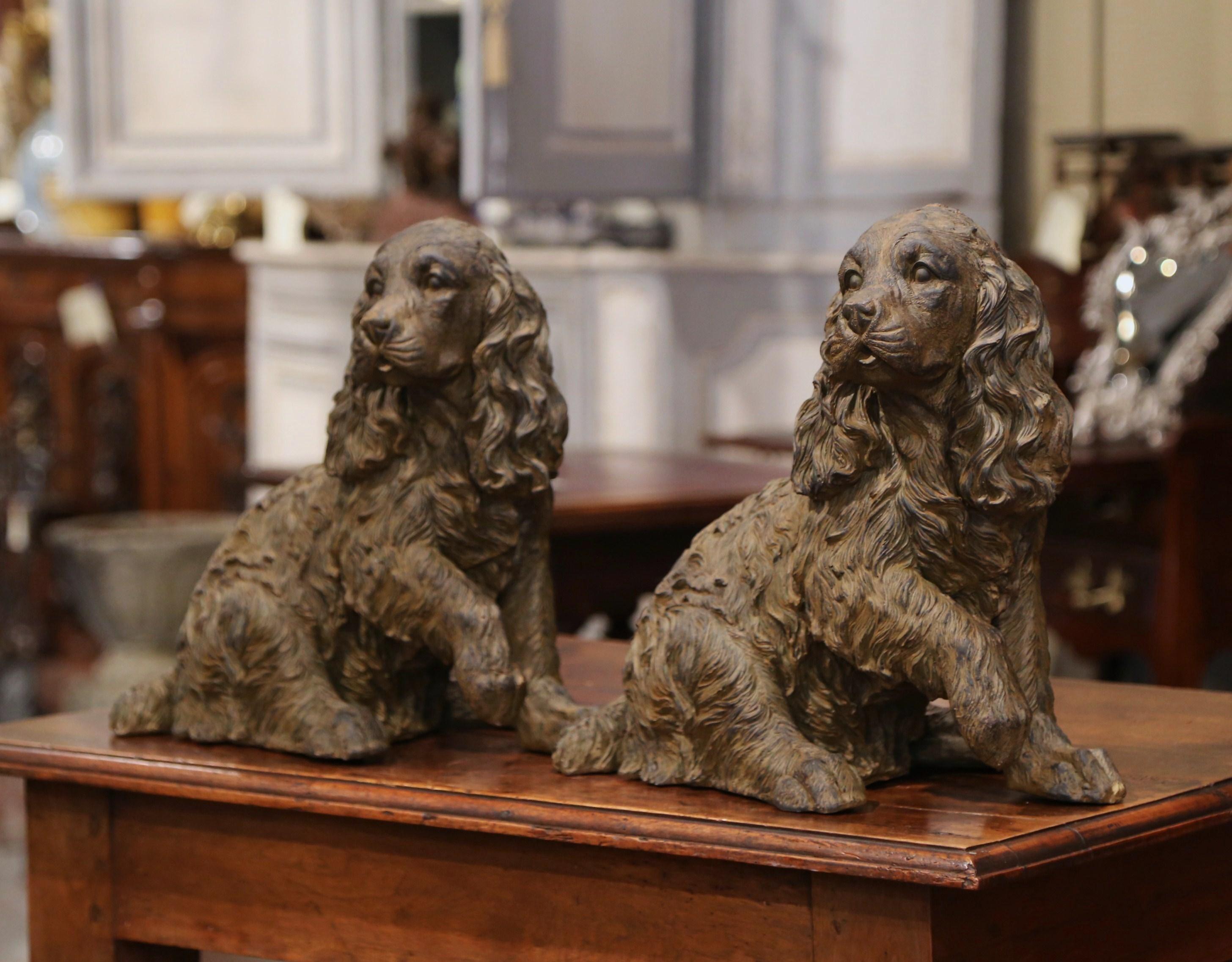 Guard an entry with this pair of charming resin Cocker Spaniel sculptures. Made in Belgium, circa 2000, the pair of dog sculptures show two matching spaniels seating on their back legs with their front right leg up. The dogs figures are in excellent