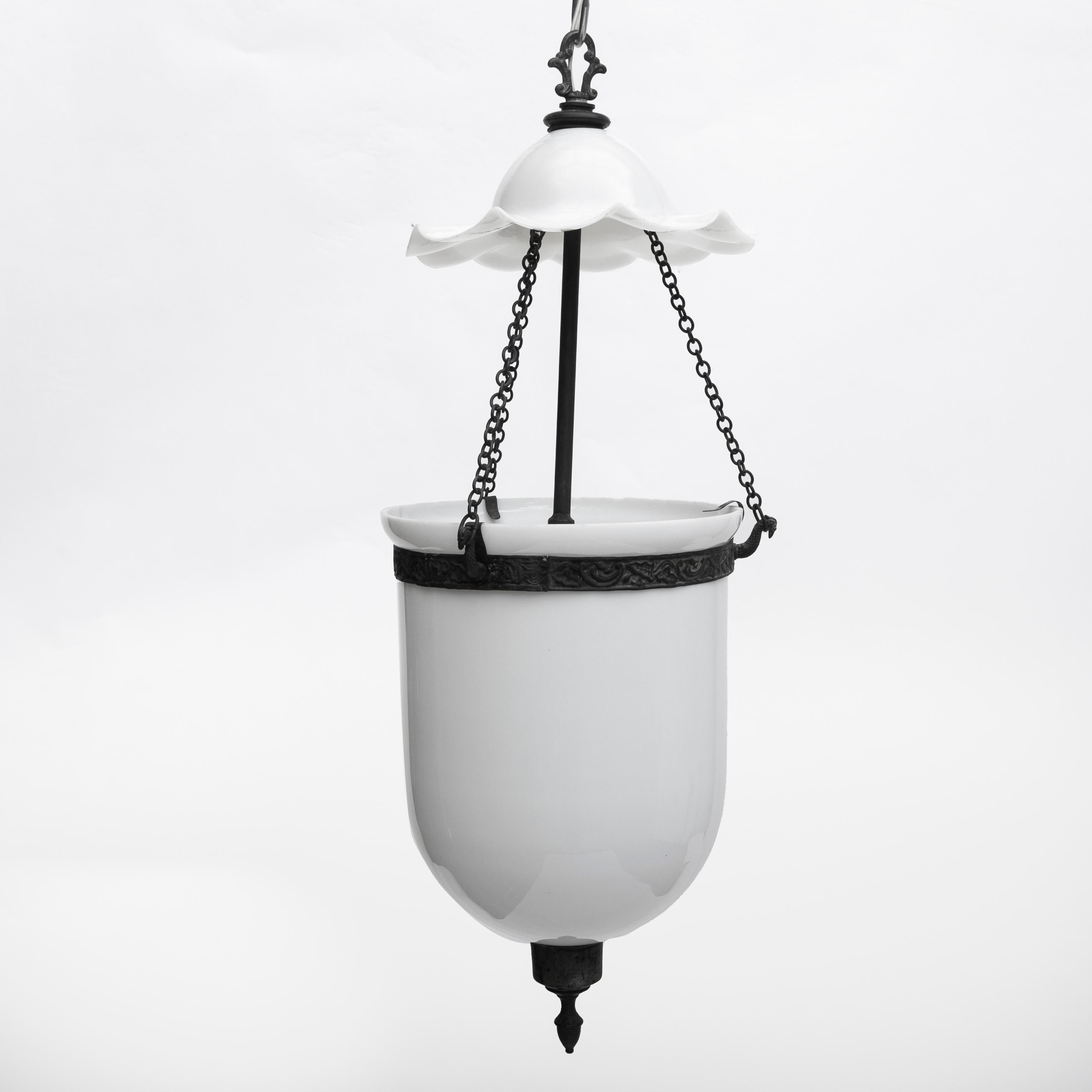 Pair of white opaline glass and patinated brass bell jar hurricane hanging lanterns.
Original patinated brass fittings, including chains, final and banding with bird's heads supporting the chains.
Bell jar and shade in white opaline glass.
Fitted