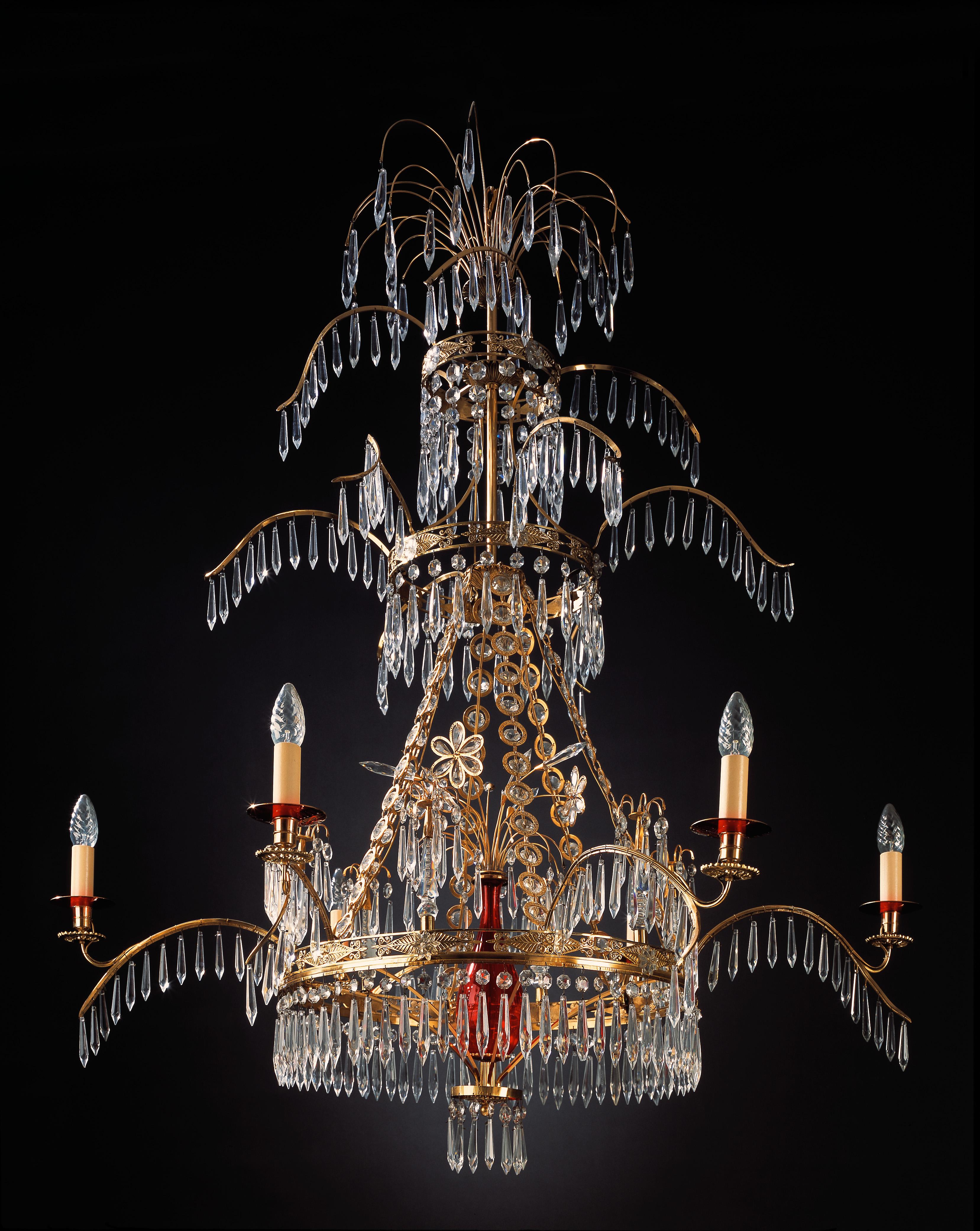 An impressive and elegant pair of Russian style neoclassical chandeliers. The circular pierced corona hung with facetted drops and suspending from chains, the main circlet issuing six branches and a central baluster-shaped red glass stem with