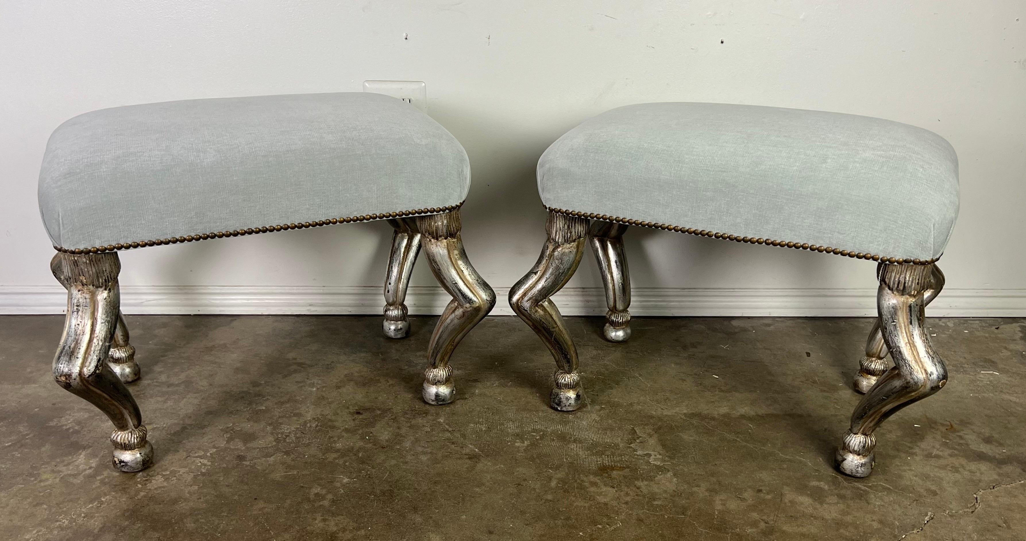 A pair of elegant benches, each enveloped in soft grayish-blue velvet, exuding a serene and sophisticated charm.  

The benches are distinguished by their four striking silver legs, each sculpted in the style of antelope legs.  They add a touch of