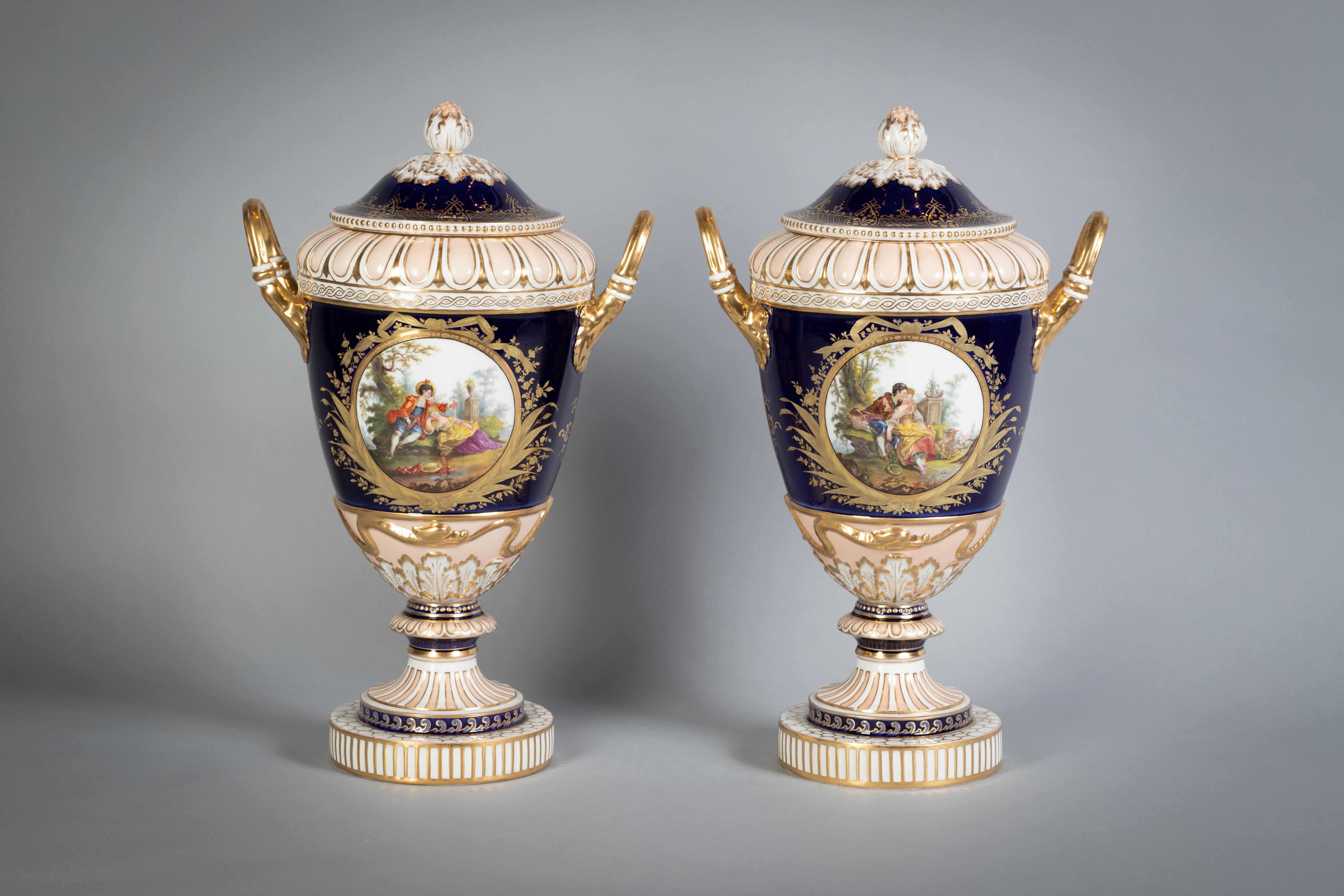 Each relief molded urn flanked by upright handles, painted with roundels with a scene of lovers on the front and back, on a cobalt blue ground.
