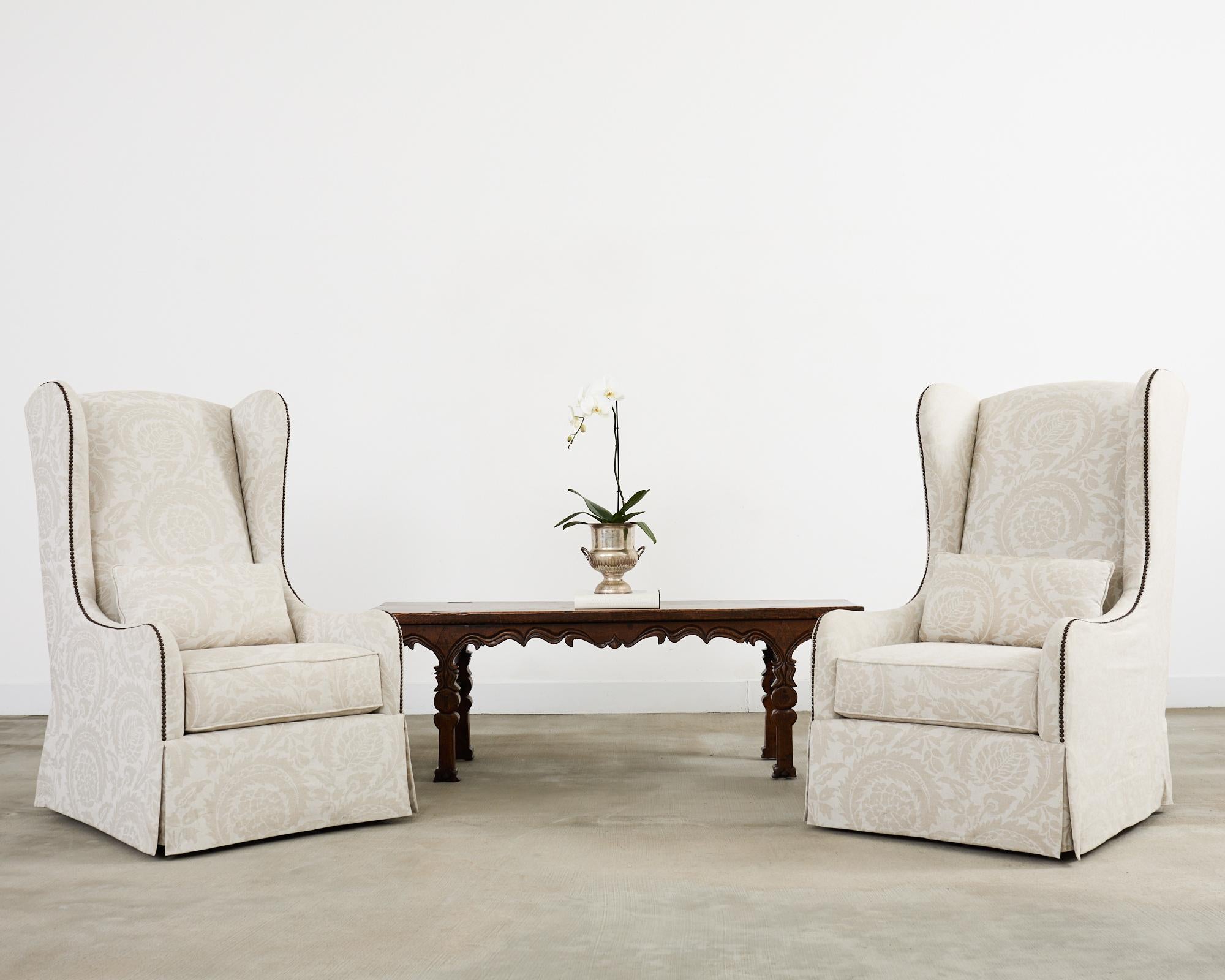 Grande paire de fauteuils à oreilles rembourrés, fabriqués sur mesure par Bernhardt. Les cadres en bois dur présentent de grandes ailes et des accoudoirs gracieusement incurvés, bordés de têtes de clous en laiton patiné. Le siège généreux est doté