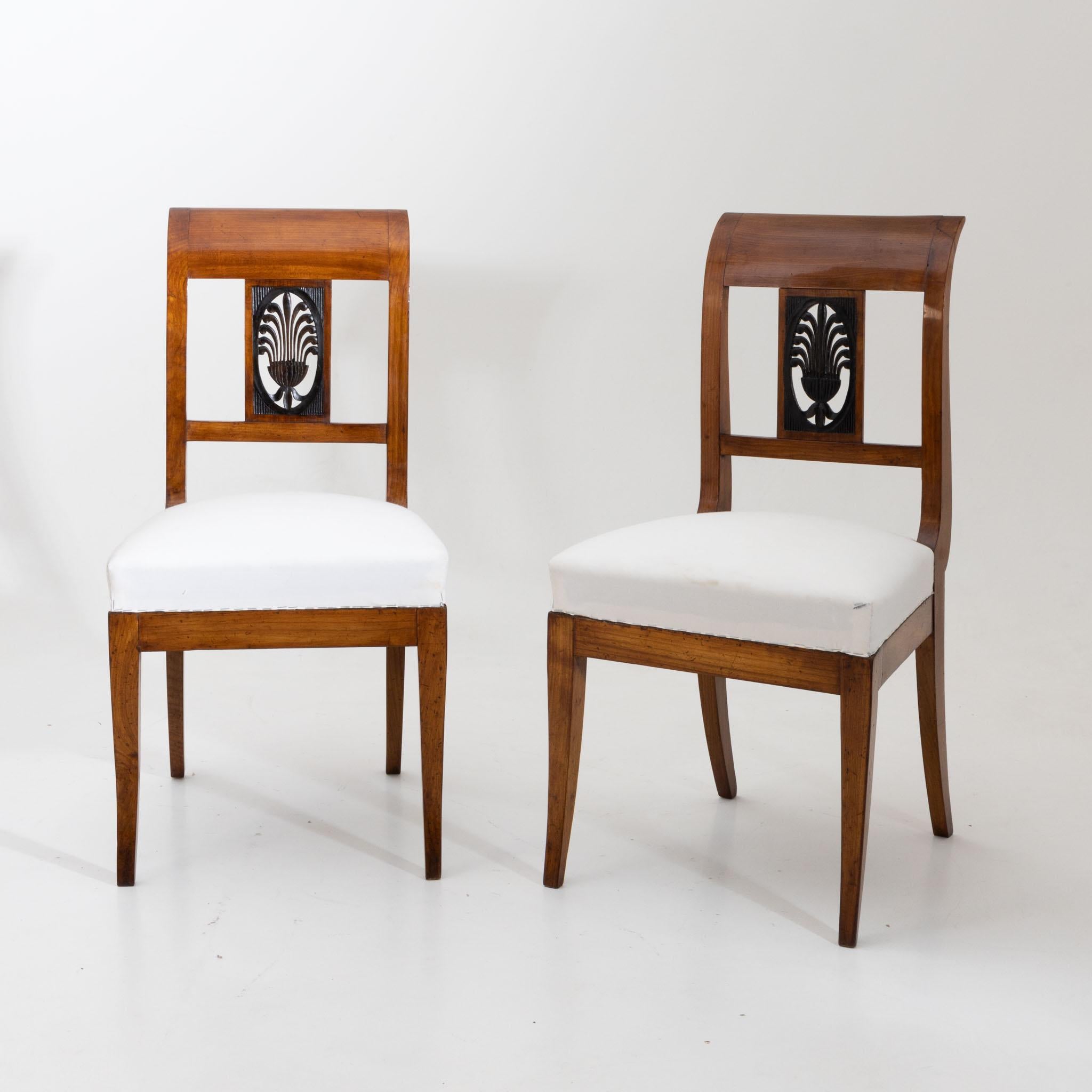 Pair of Biedermeier chairs of solid cherry with white seat and openwork backrest with dark stained reed leaf decoration. The chairs have been newly upholstered and hand polished.
