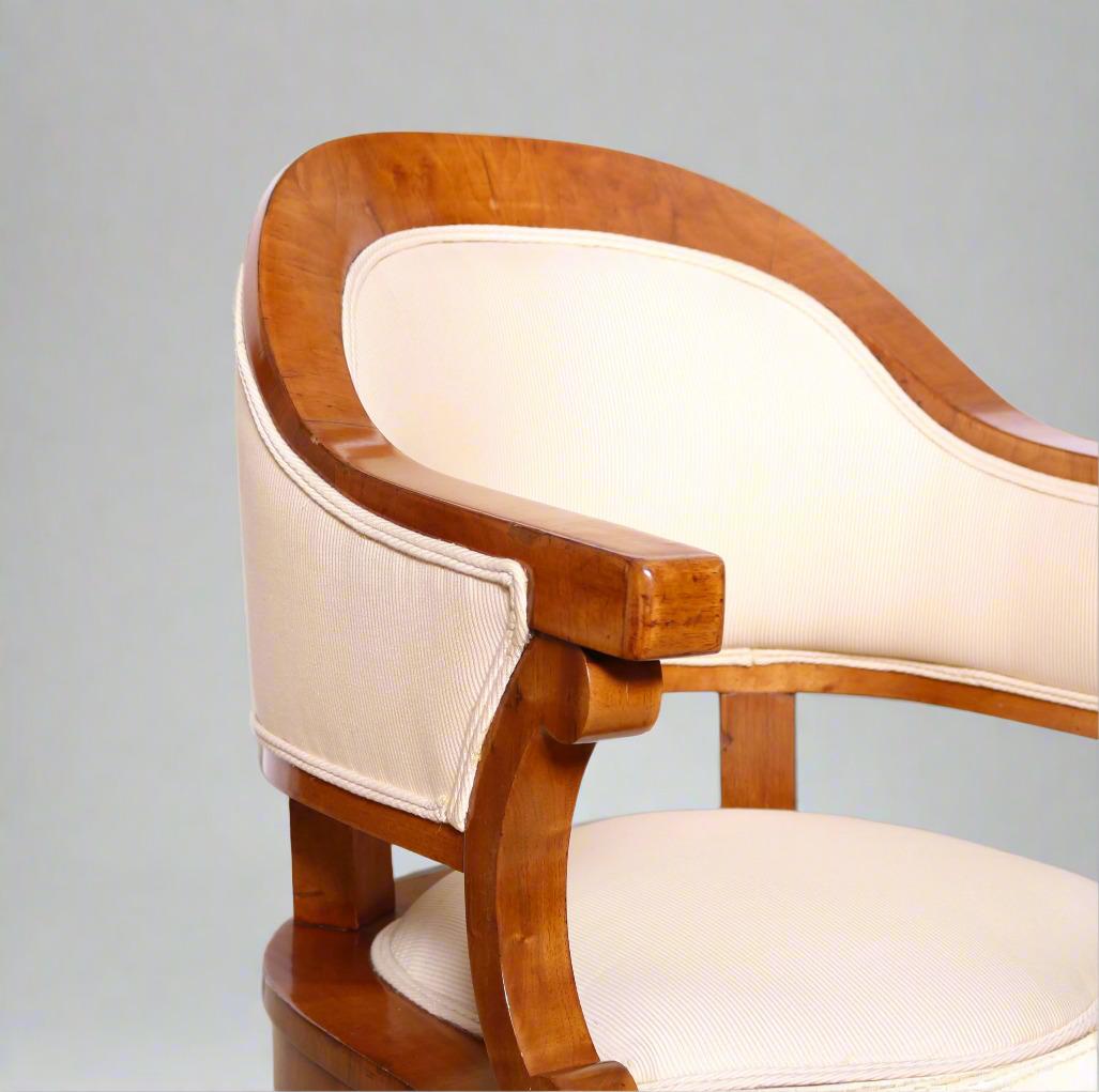 Paire de fauteuils Biedermeier en merisier. Une magnifique traverse de crête sculptée s'insère en douceur dans la partie supérieure de l'accoudoir, soutenue par des volutes en 