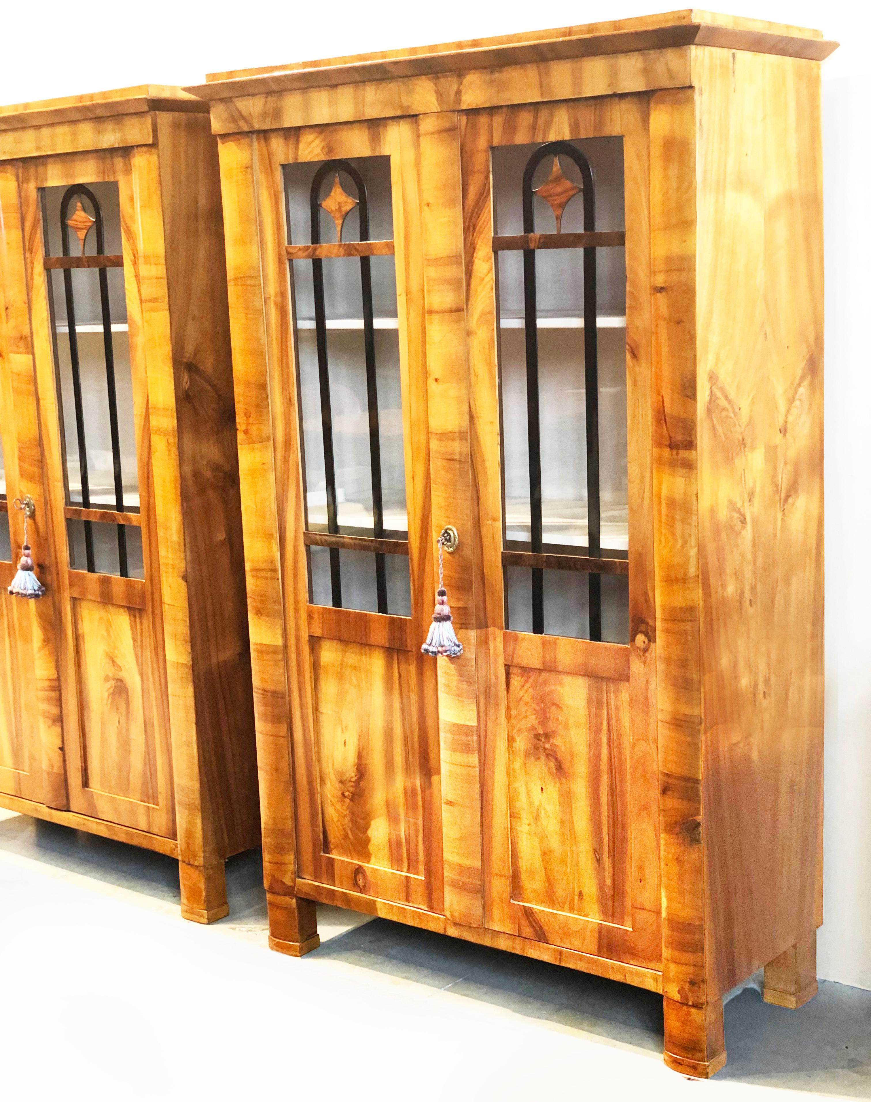 Outstanding and rare pair of early 19th century bookcases / display cabinets of finely figured north European blond walnut exterior. Each display cabinet features 3 slightly curved frontal columns, two of them on each side terminating in block feet