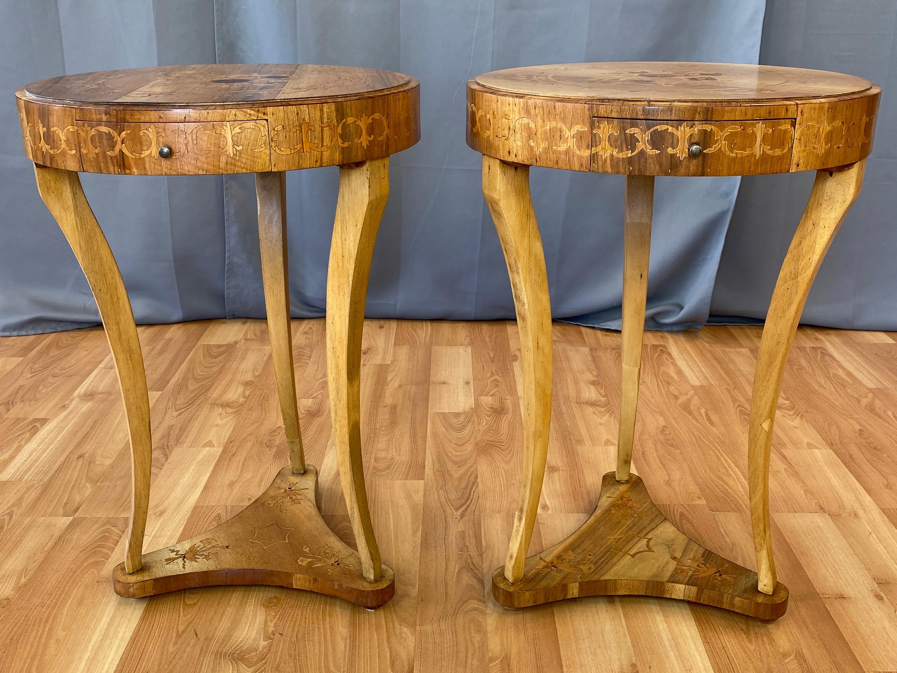 A delightful pair of 1940s Italian Biedermeier-style marquetry side or end tables with drawer.

Round top with beautifully executed fruitwood and rosewood floral & ribbon motif marquetry. Supported by a trio of lithe curved legs that stand on a