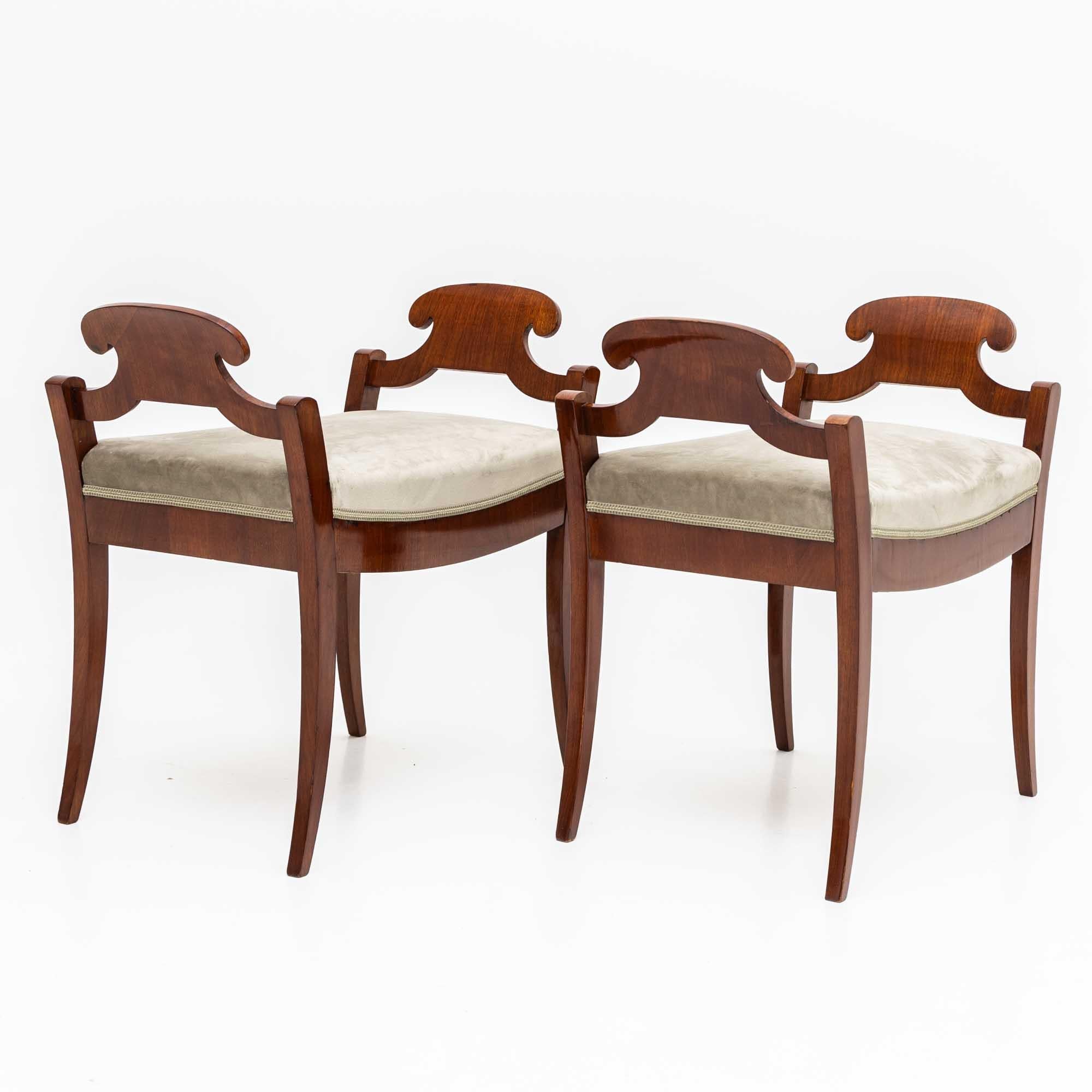 Una coppia decorativa di tabouret del XIX secolo con eleganti gambe a sciabola e braccioli smerlati. Gli sgabelli sono impiallacciati in mogano e sono stati rivestiti con gusto in un tessuto vellutato beige.