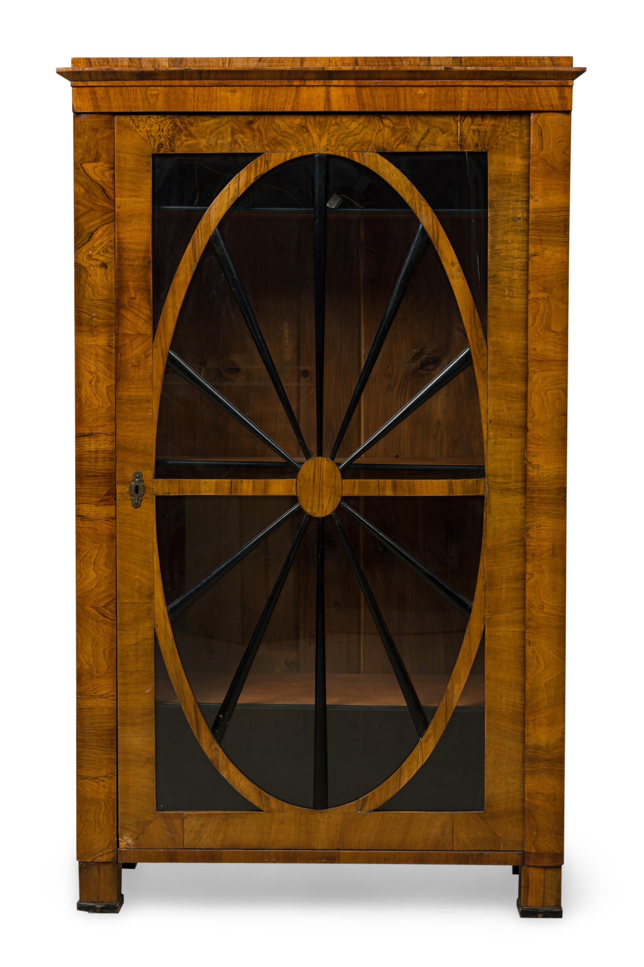 PAIR of Biedermeier (19th Century) walnut bookcase / display cabinets featuring oval glass front doors with an ebonized wheel wood pane design, having three adjustable interior shelves and top-mounted (modern) interior lights, resting on four block