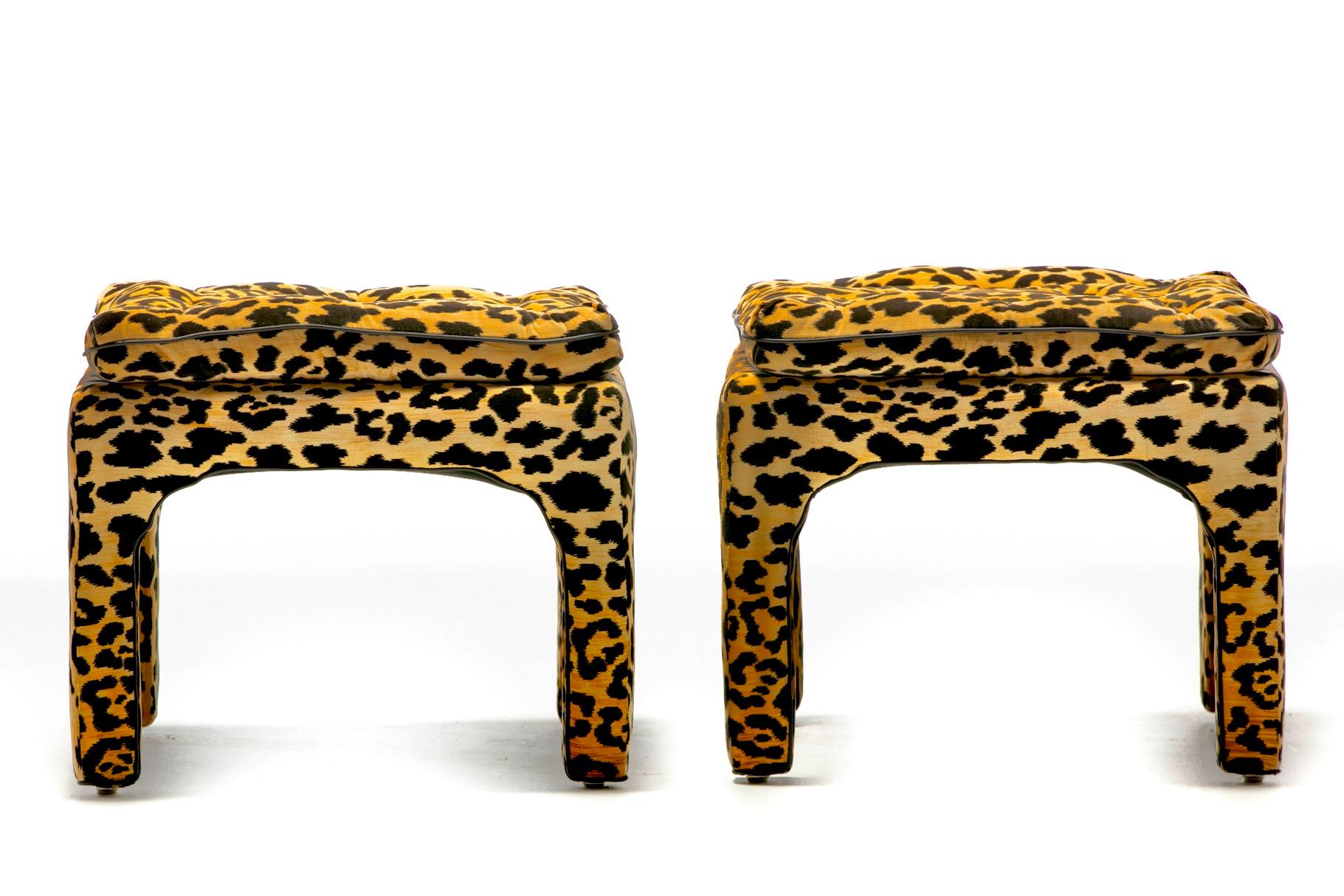 Super sexy pair of 1970s Billy Baldwin style ottomans or stools fully restored with new cushioning and upholstered in sultry leopard velvet with black leather piping detail. Chic. Sexy. Lux look and vibe. Tufted leopard velvet top cushion is