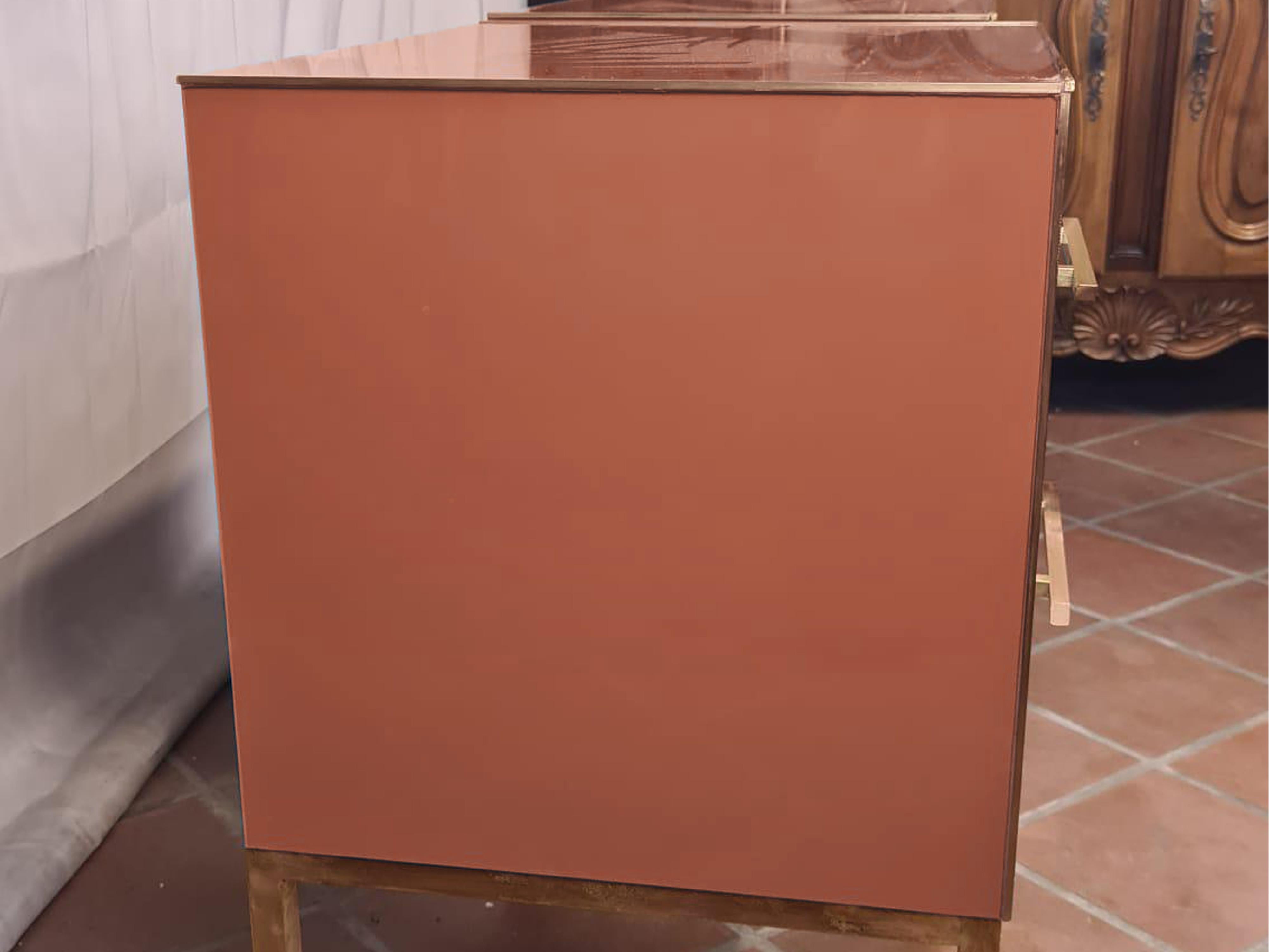 This pair of Birch side tables elegantly captures the essence of 1950s style with a modern twist. 

Made of solid birch and embellished with red beige mirrored glass, these side tables feature refined vertical brass inserts along the drawers,