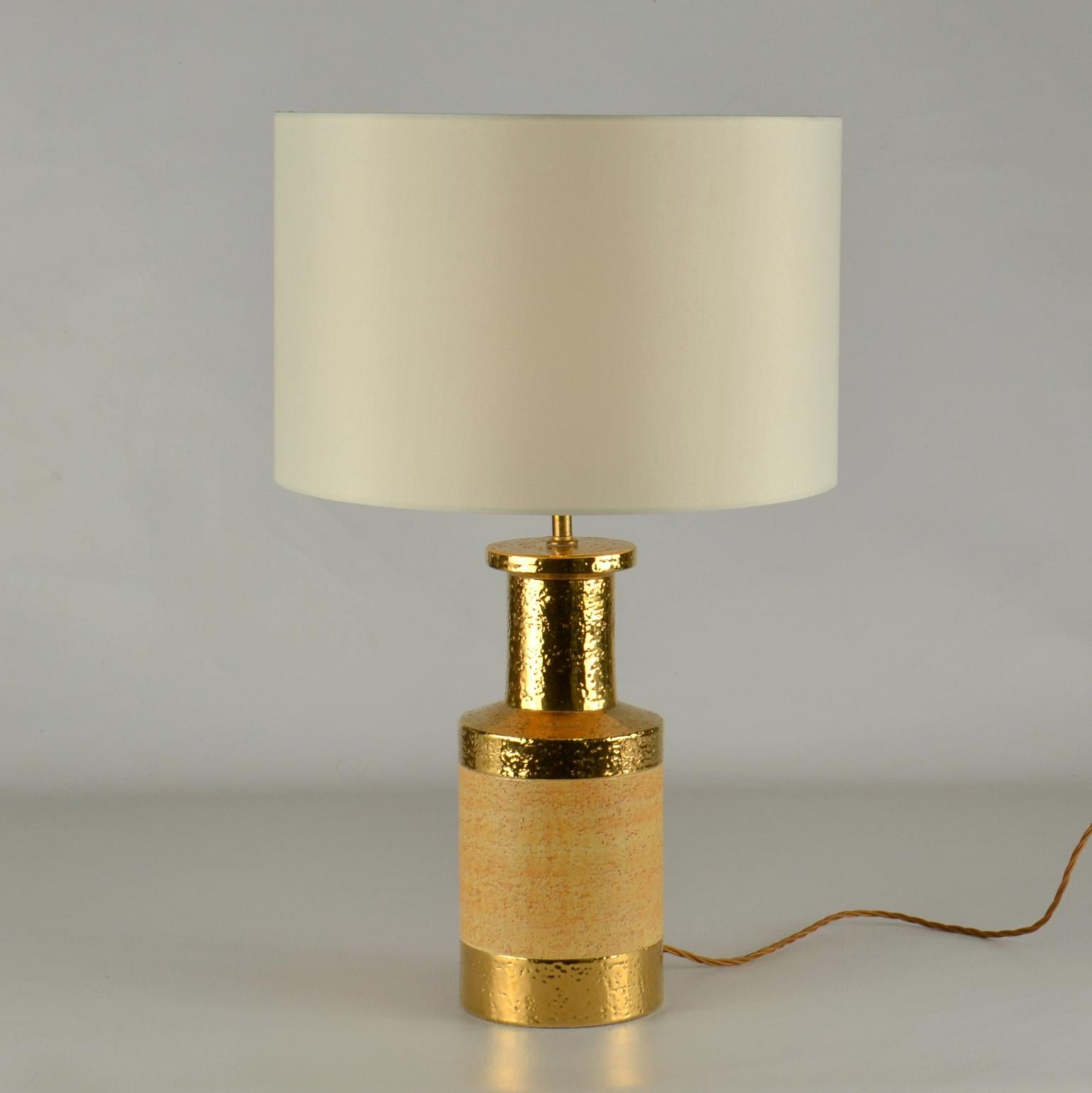 Bitossi cylinder shape table lamps where produced in stoneware with a natural glaze. The border at the neck is gilded, the band of shiny gold emphasis the rough texture of the ceramic body.
Guido Bitossi established his own ceramic workshop near