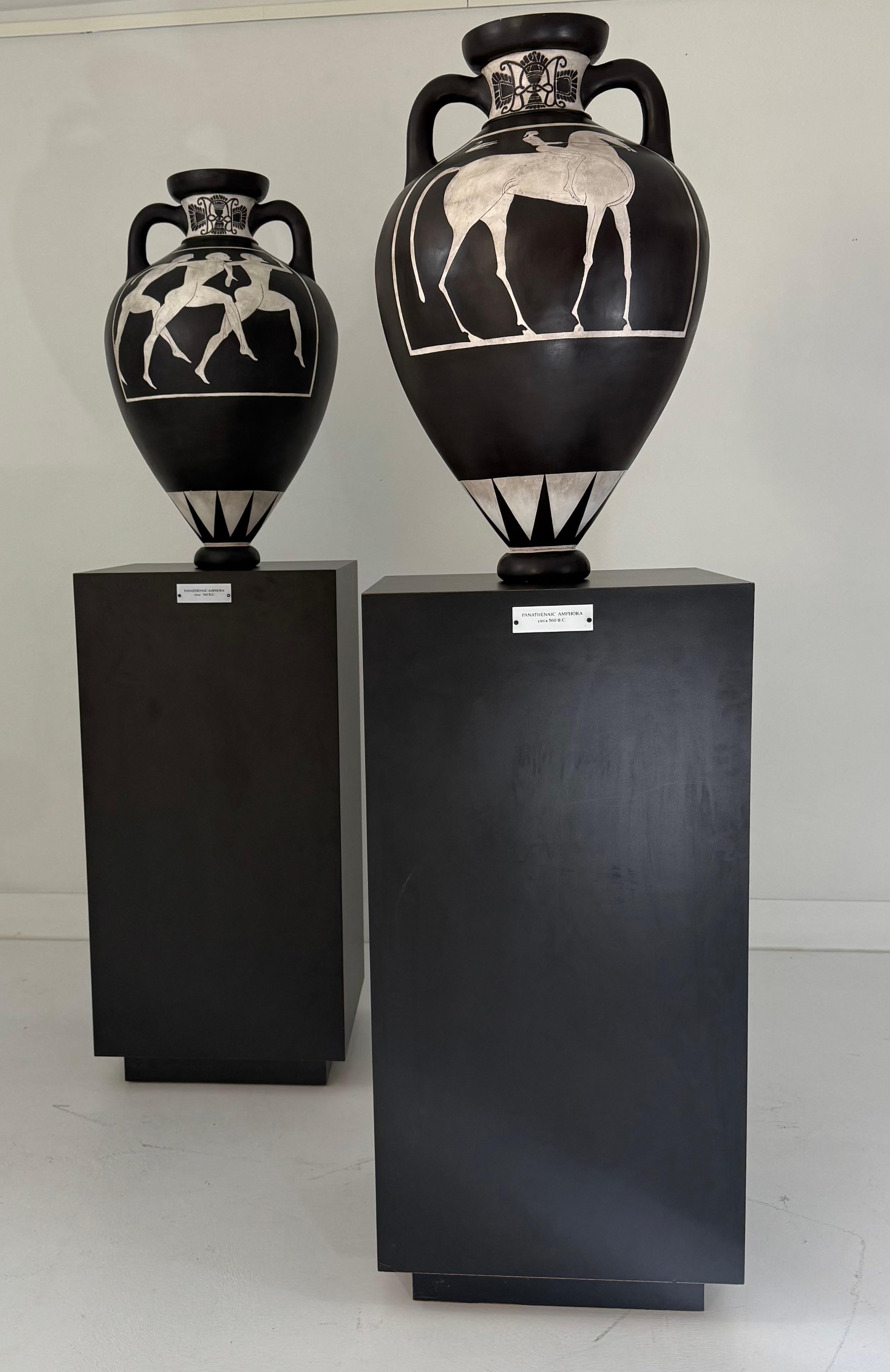 Striking and sculptural, this pair of monumental amphoras is a modern homage to the Panathenaic prize vessels of ancient Athens. Each amphora features iconic black-figure-inspired motifs—one depicting athletic nude male figures in motion, the other