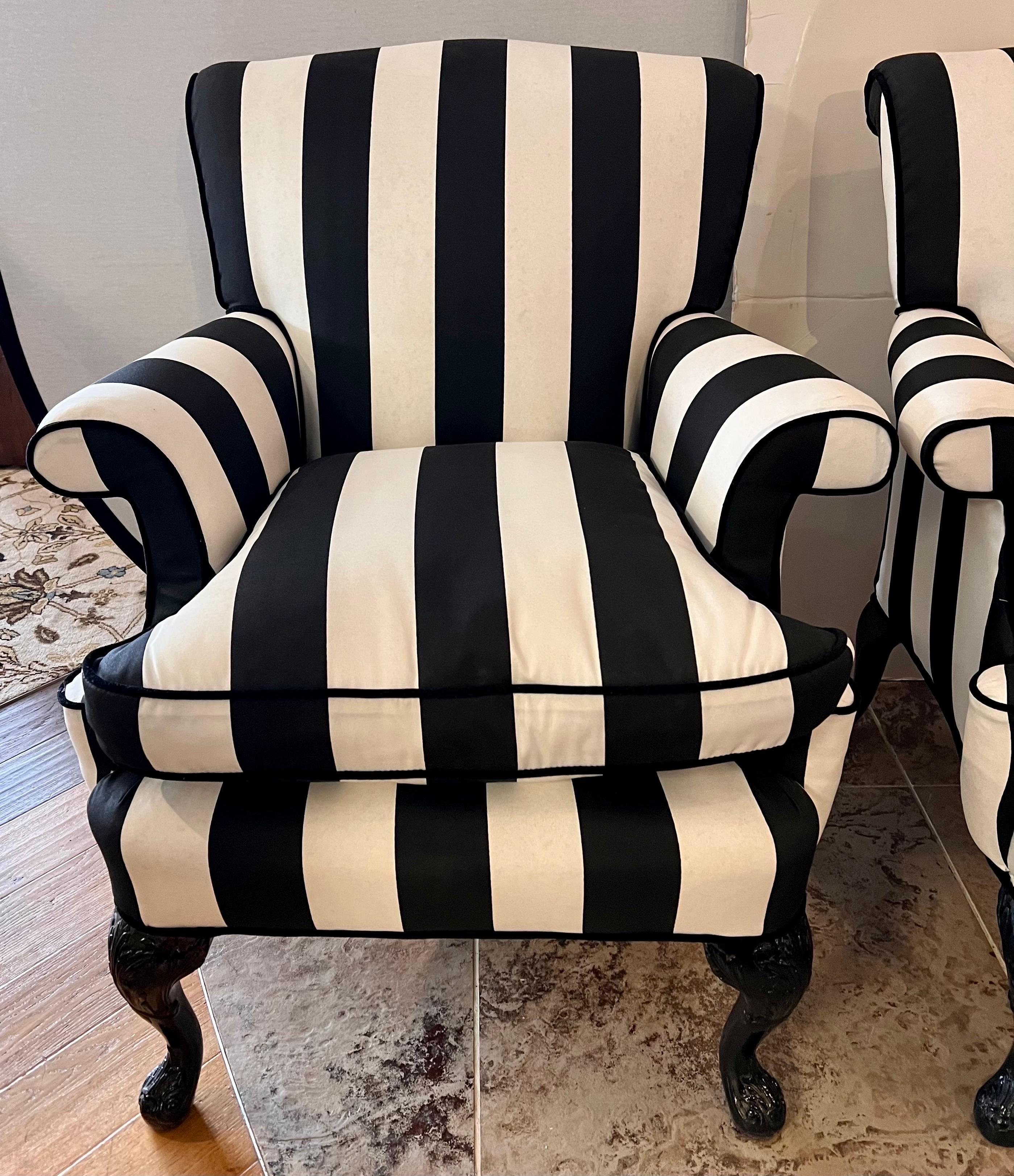 Elegant matching pair of French bergeres that have been recently upholstered in a bold black and white stripe fabric. Features rolled back and arms and black lacquered carved legs.
