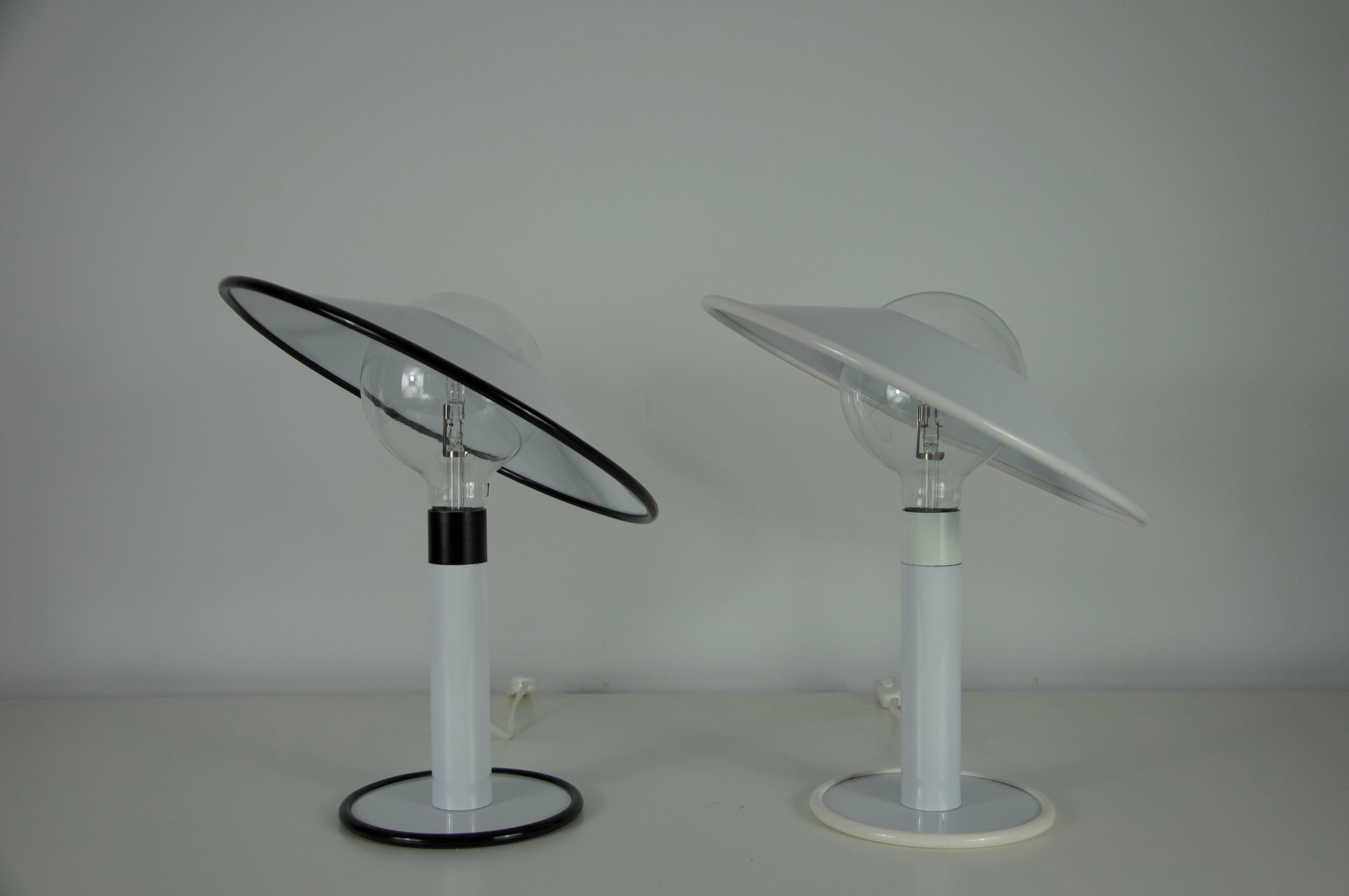 Cette paire de lampes de table blanches datant de l'Italie des années Whiting présente un design postmoderne à la fois ludique et fonctionnel. Chaque lampe est dotée d'une élégante base cylindrique en métal laqué blanc, supportant un grand abat-jour