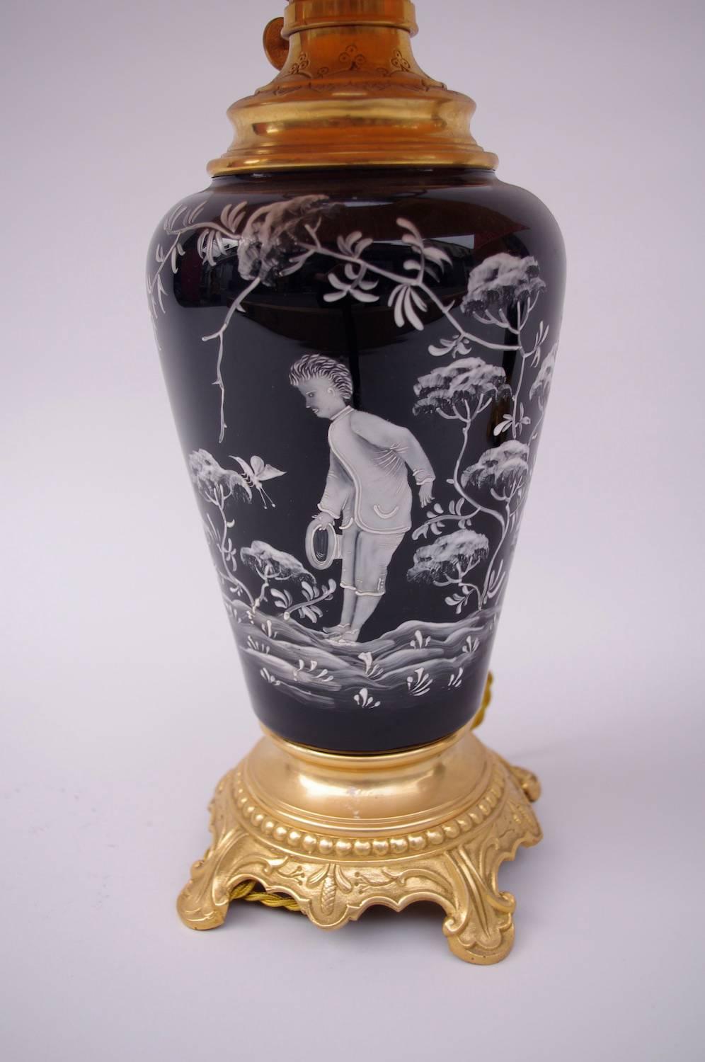 Pair of black enameled opaline lamps in vase shape. Round chiselled and gilt bronze mount with a pearls frieze, standing on four acanthus-shape legs.
White-painted enamel decoration of scenes representing a young boy walking through the vegetation