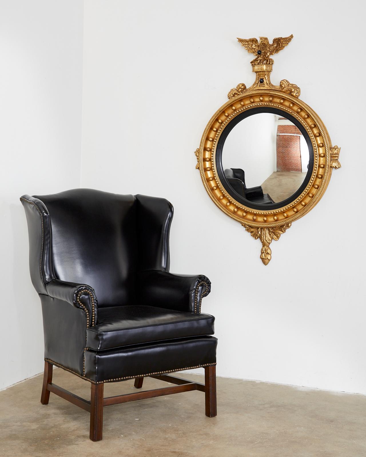 Sleek pair of English Georgian style wing chairs or wingbacks featuring black patent leather style naugahyde upholstery. Beautifully crafted mahogany frames with fully developed wings and brass tack nail heads borders. Supported by square reeded