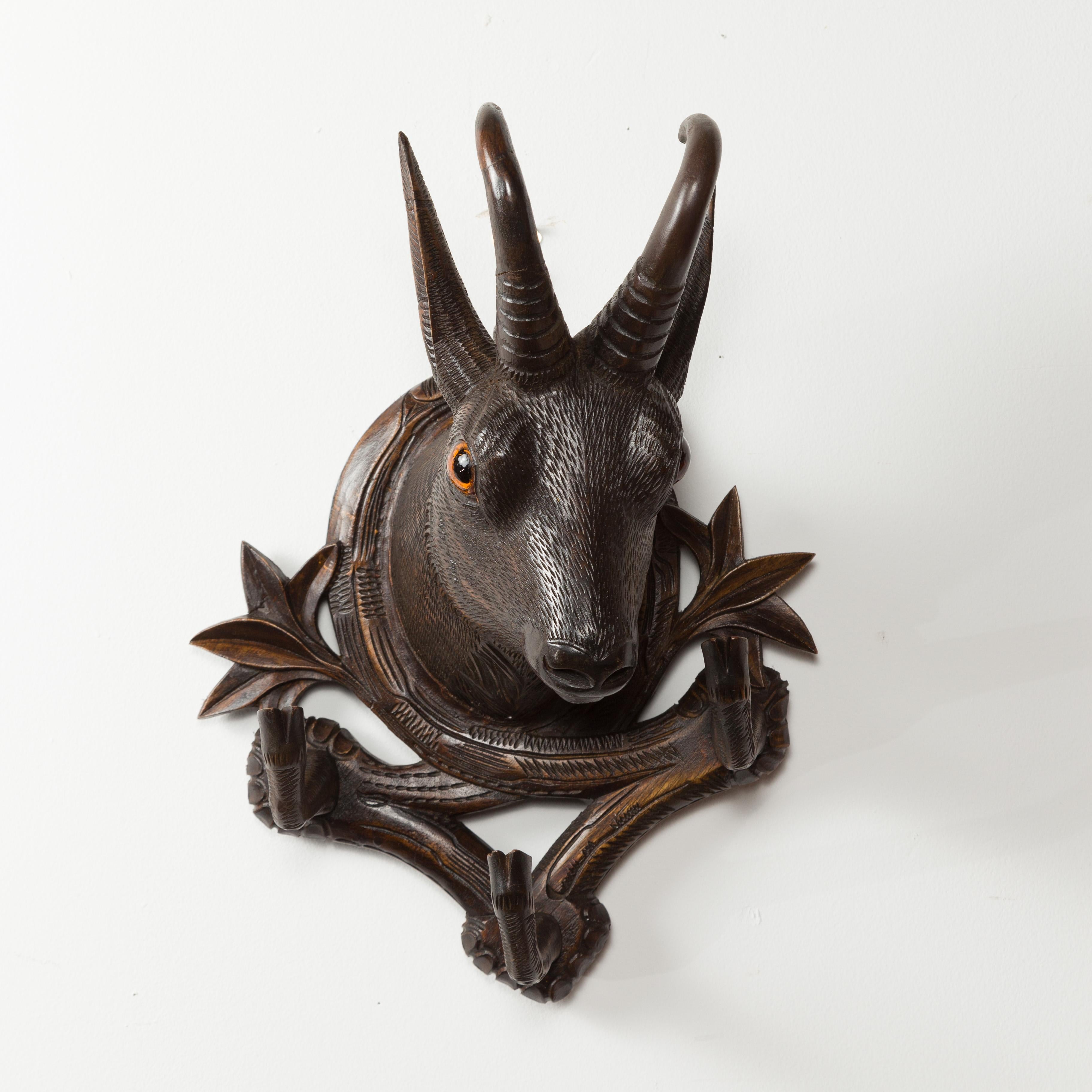 A pair of Black Forest carved wooden chamois heads hat or coat racks from the late 19th century, with foliage accents. Created during the last quarter of the 19th century, each of this pair of racks features a chamois head with glass eyes, emerging