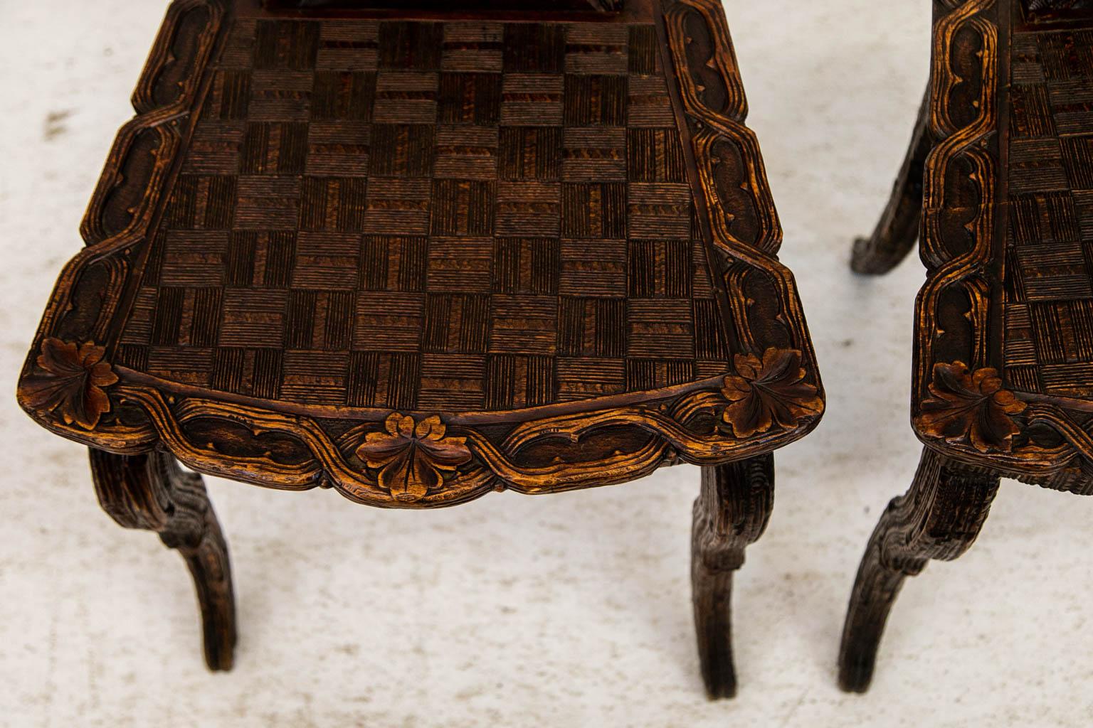 This pair of hall chairs are carved with floral and leaf motifs on a stipled background. The seat is carved with an incised square basketweave pattern which is framed on three sides with a carved interlaced vine. The legs are carved on all four
